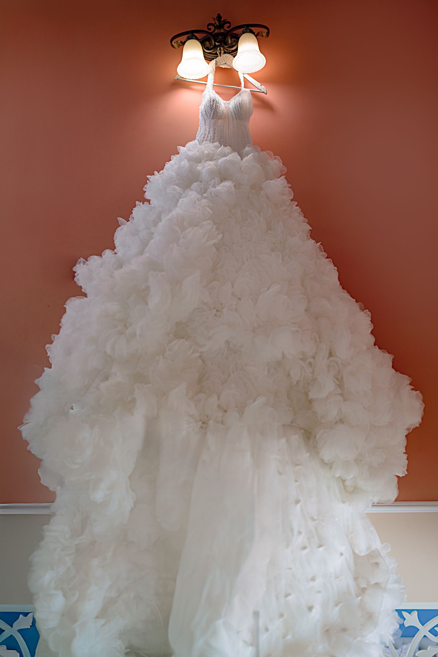 Luxurious white wedding gown with voluminous ruffled skirt displayed against red wall.