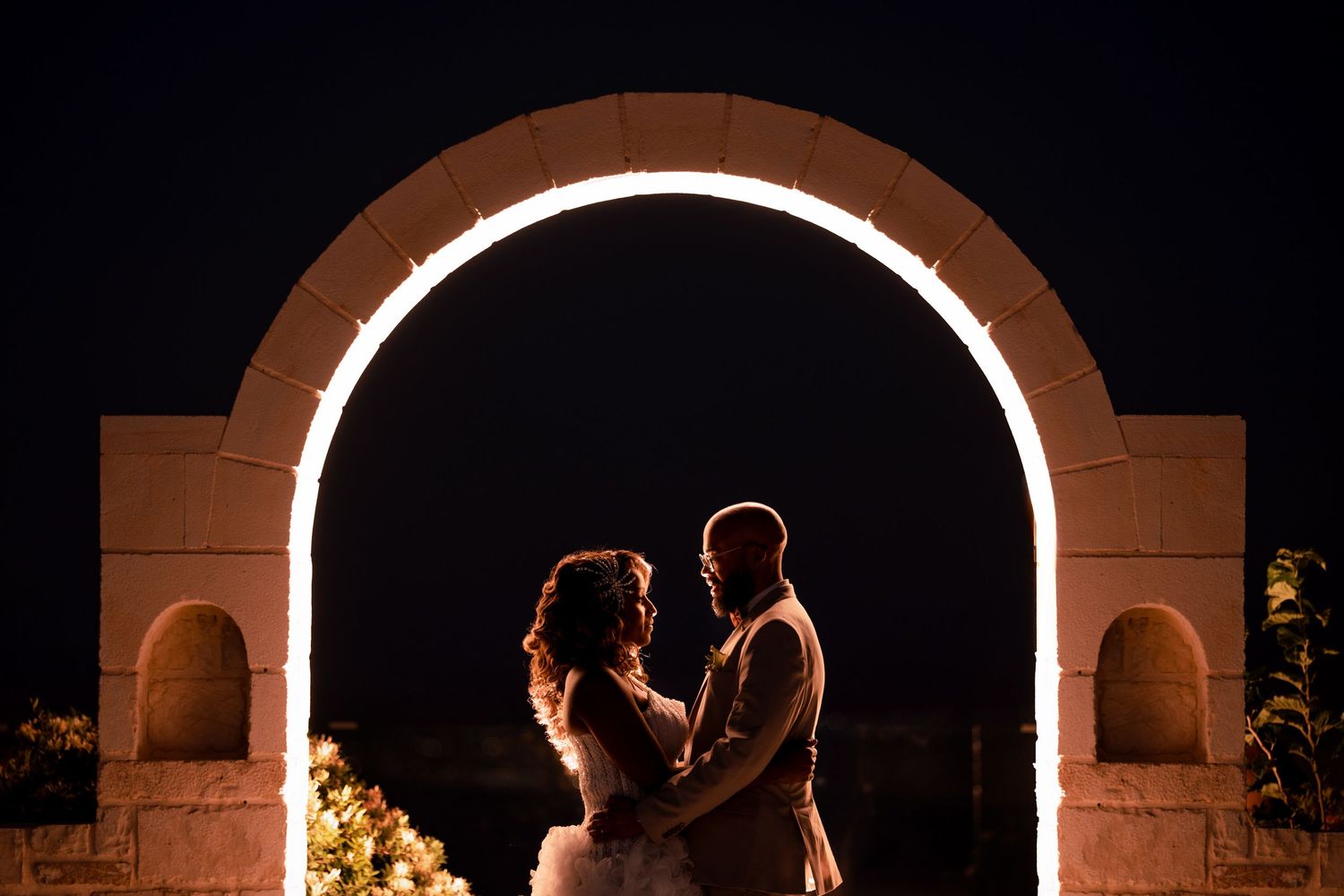 Romantic silhouettes framed within illuminated archway at night.