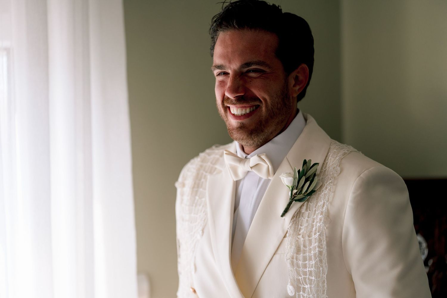 Wedding preparation scene with groom in white tuxedo jacket and boutonniere.