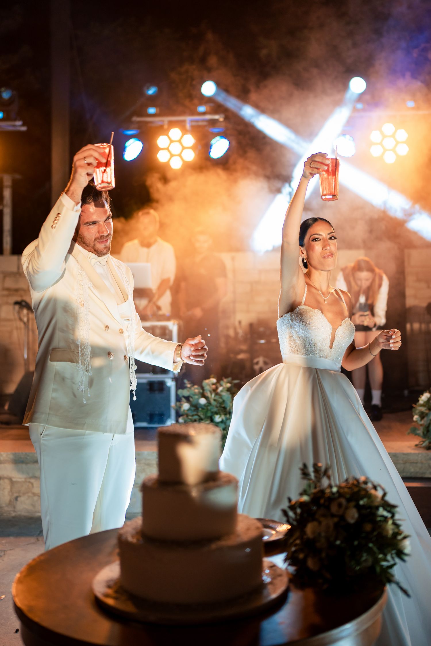 Wedding couple toasts with champagne during their reception under orange stage lighting.