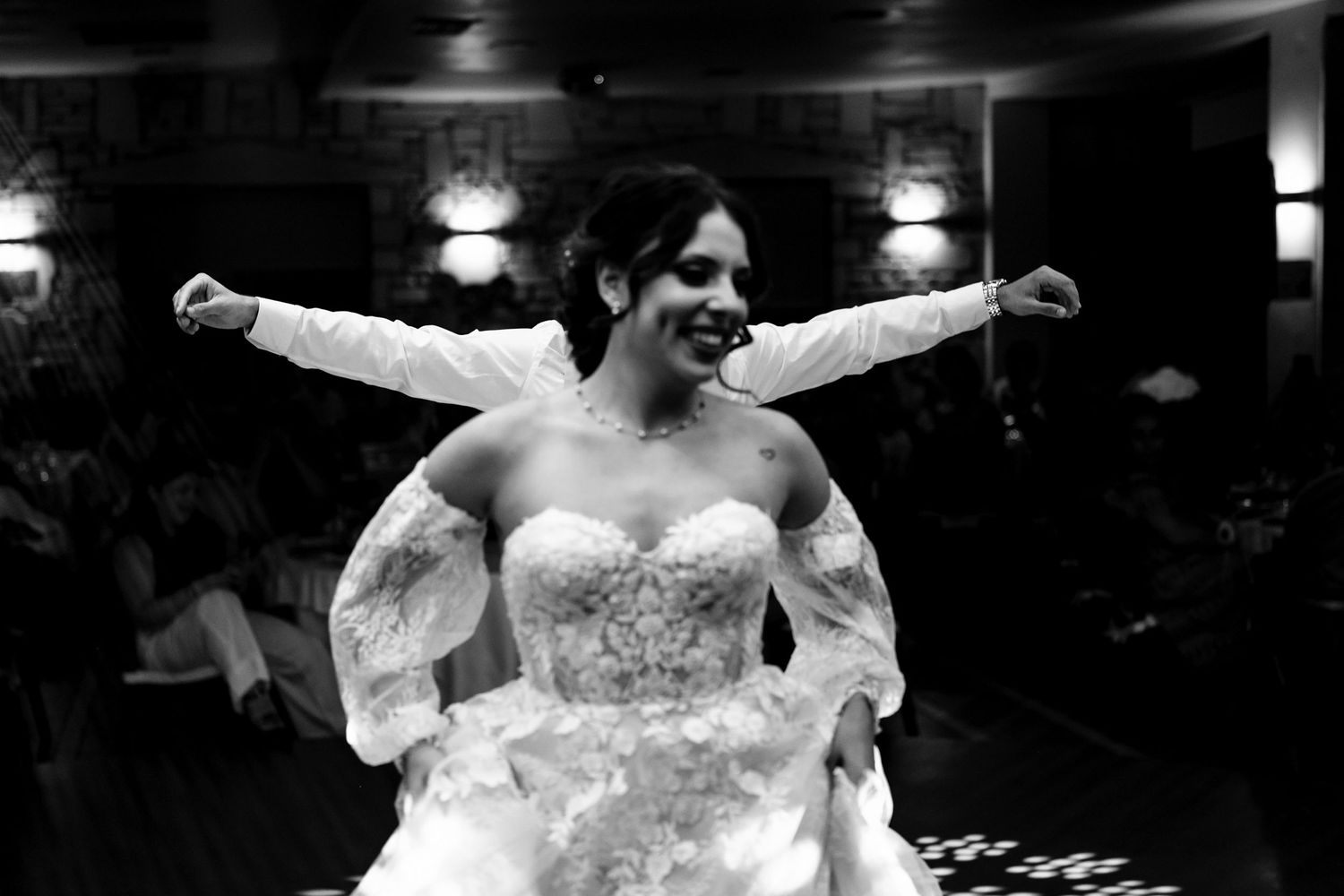 Black and white photo captures joyful dancing moments at an indoor wedding reception.