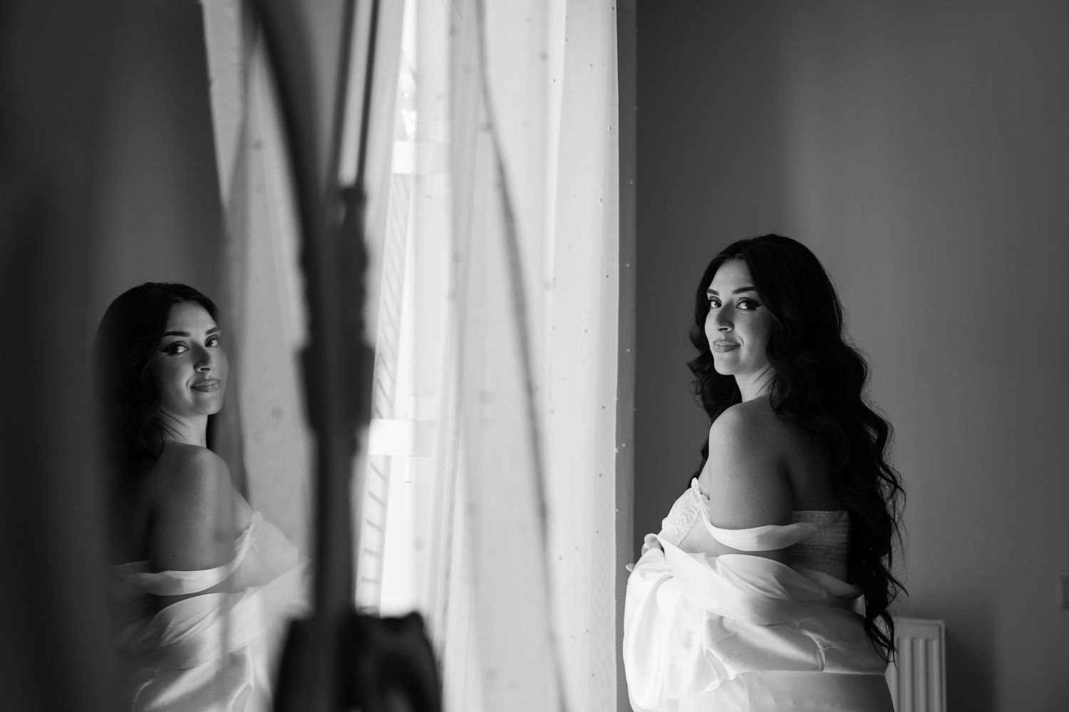 Silhouetted figure by window in dramatic black and white photography.