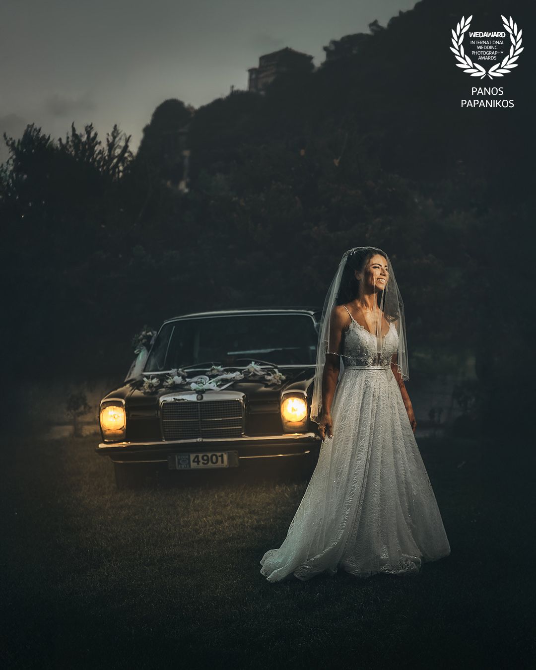 Elegant wedding dress silhouette against vintage car in moody evening lighting.