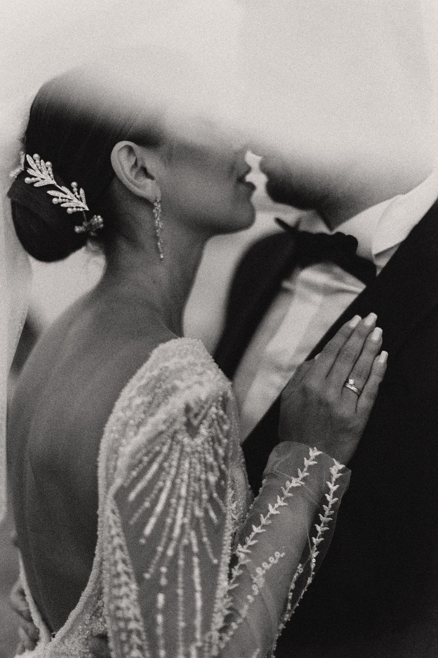 Black and white detail shot of bride's beaded gown with veil creating artistic composition.