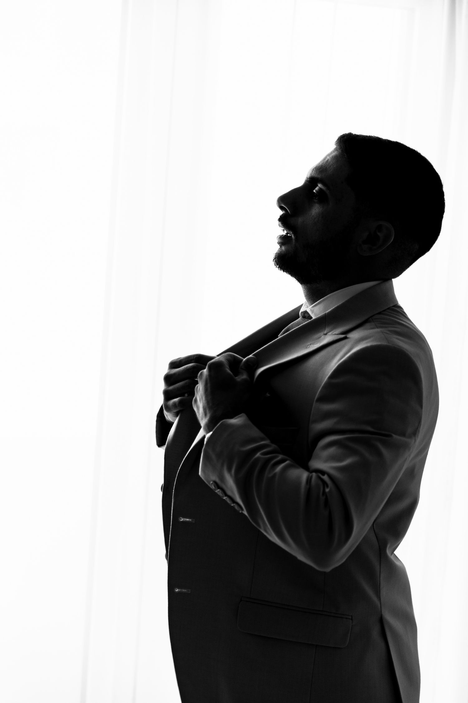 Dramatic black and white silhouettes of someone adjusting their tie against a bright background.
