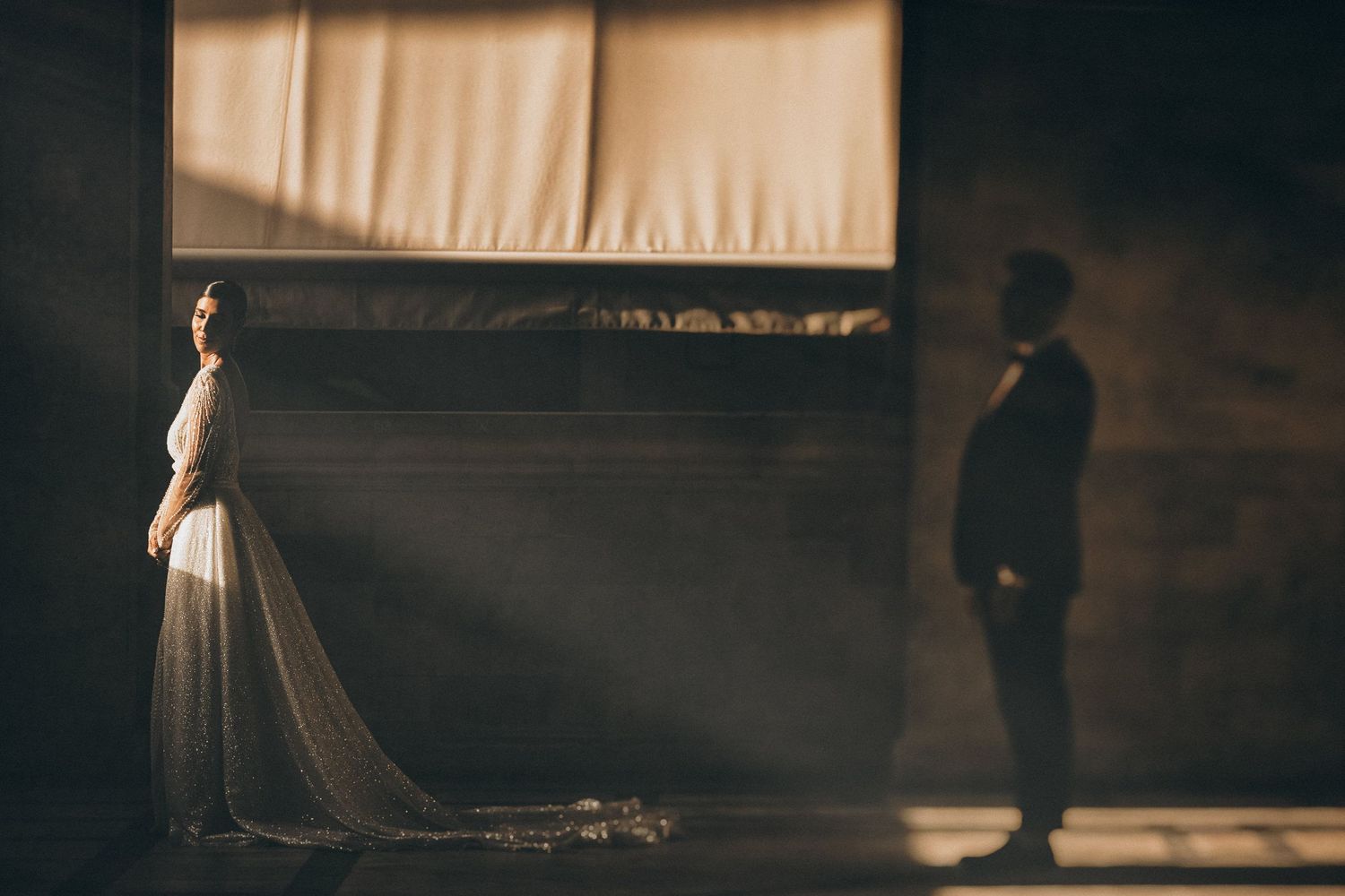 A dramatic silhouette of a bride and groom in a sunlit room with flowing curtains.