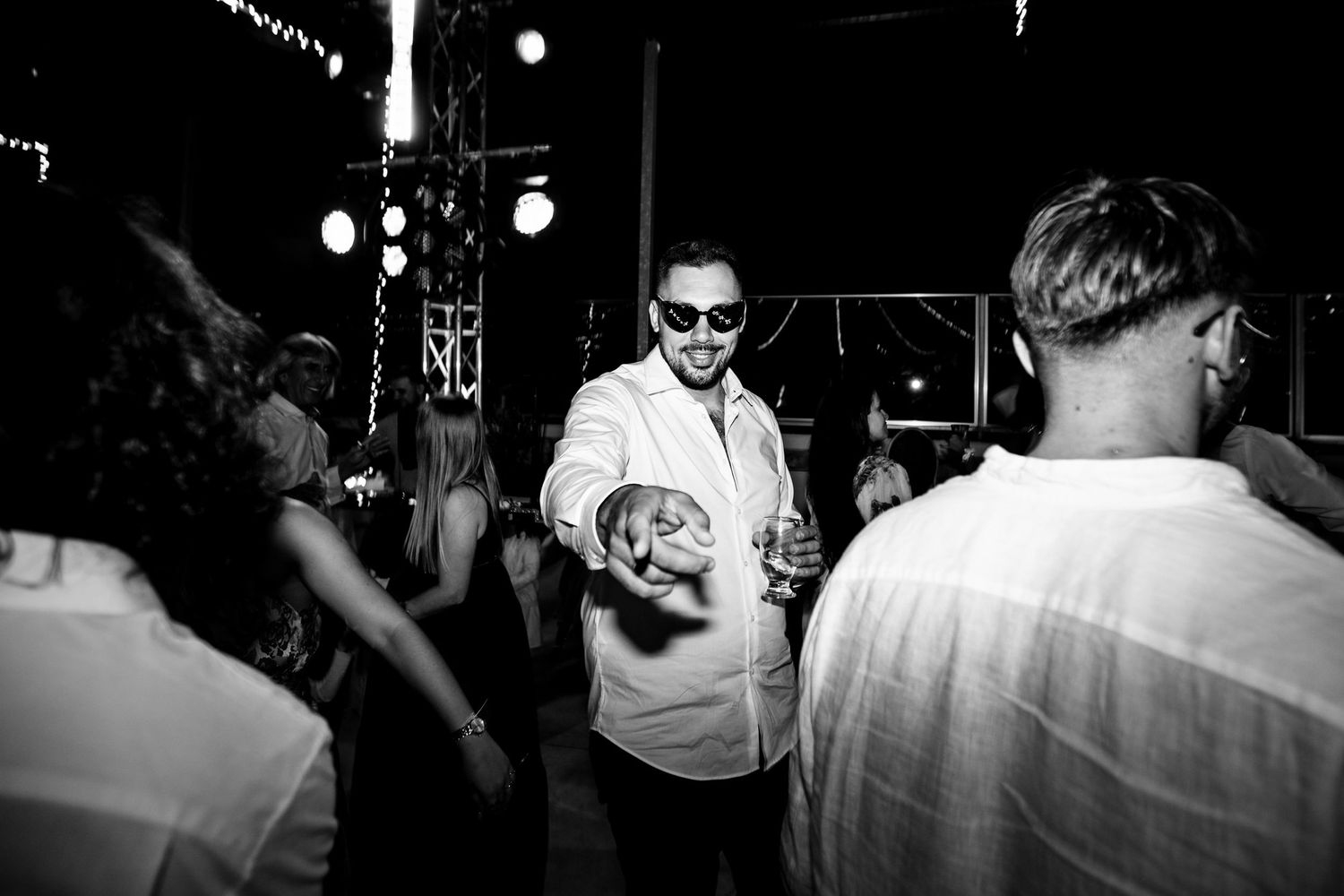 Black and white photo of a crowded dance floor with overhead lighting creating dramatic shadows.