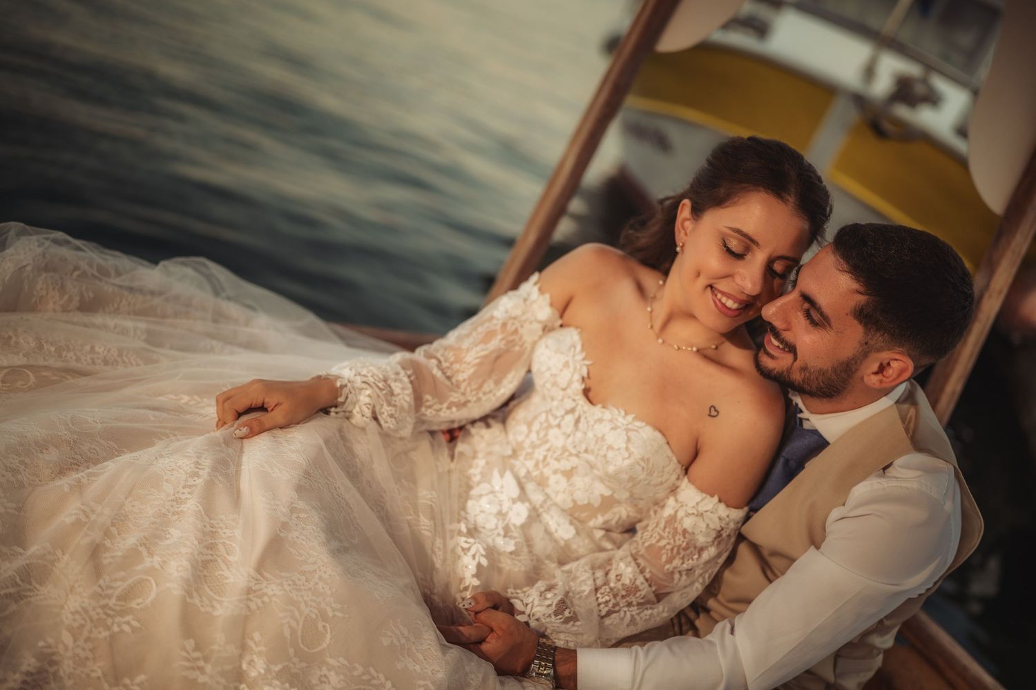 Wedding couple shares intimate moment by waterfront at sunset.