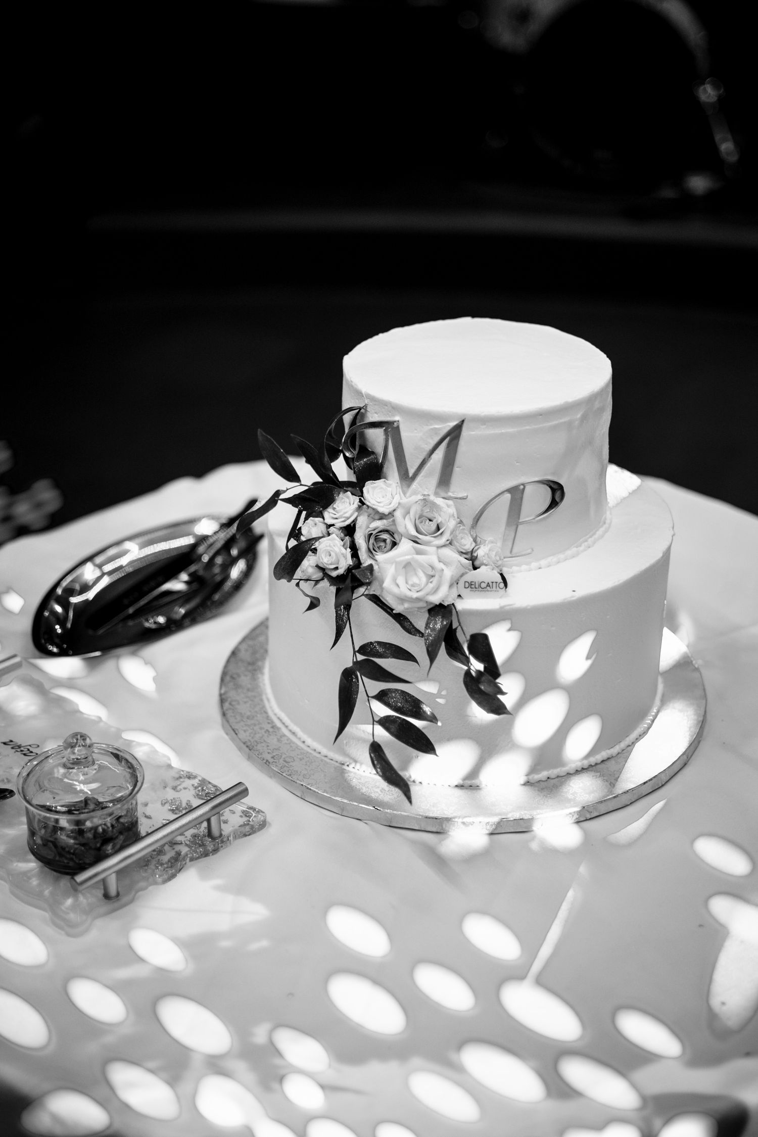 Elegant white wedding cake with floral decorations on display table with patterned lighting.