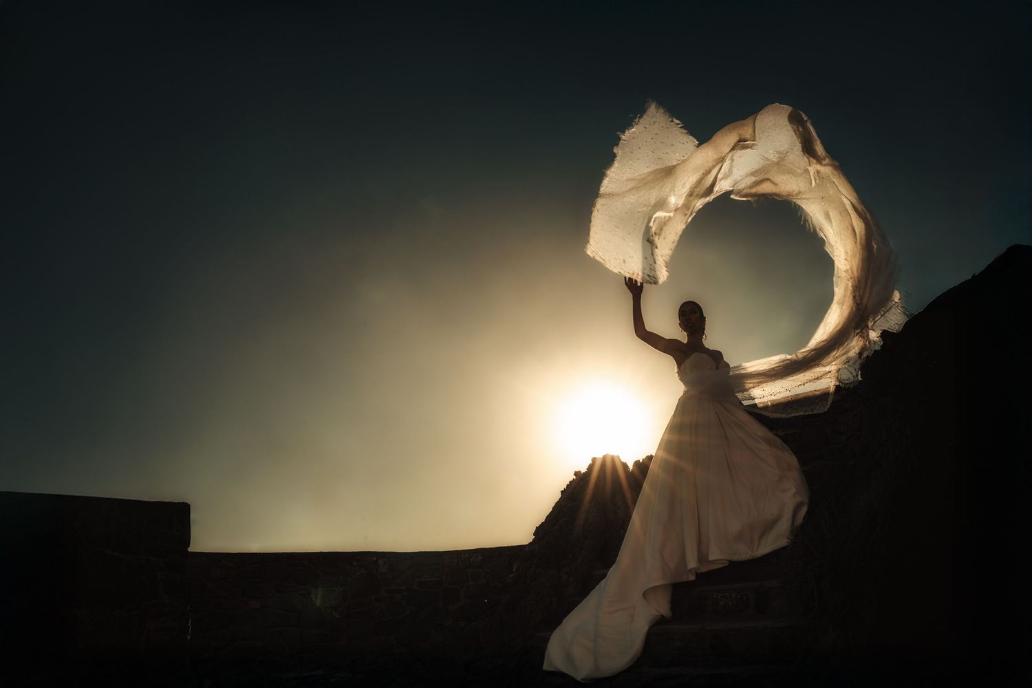 Silhouette of flowing wedding dress catches wind against dramatic evening sky.