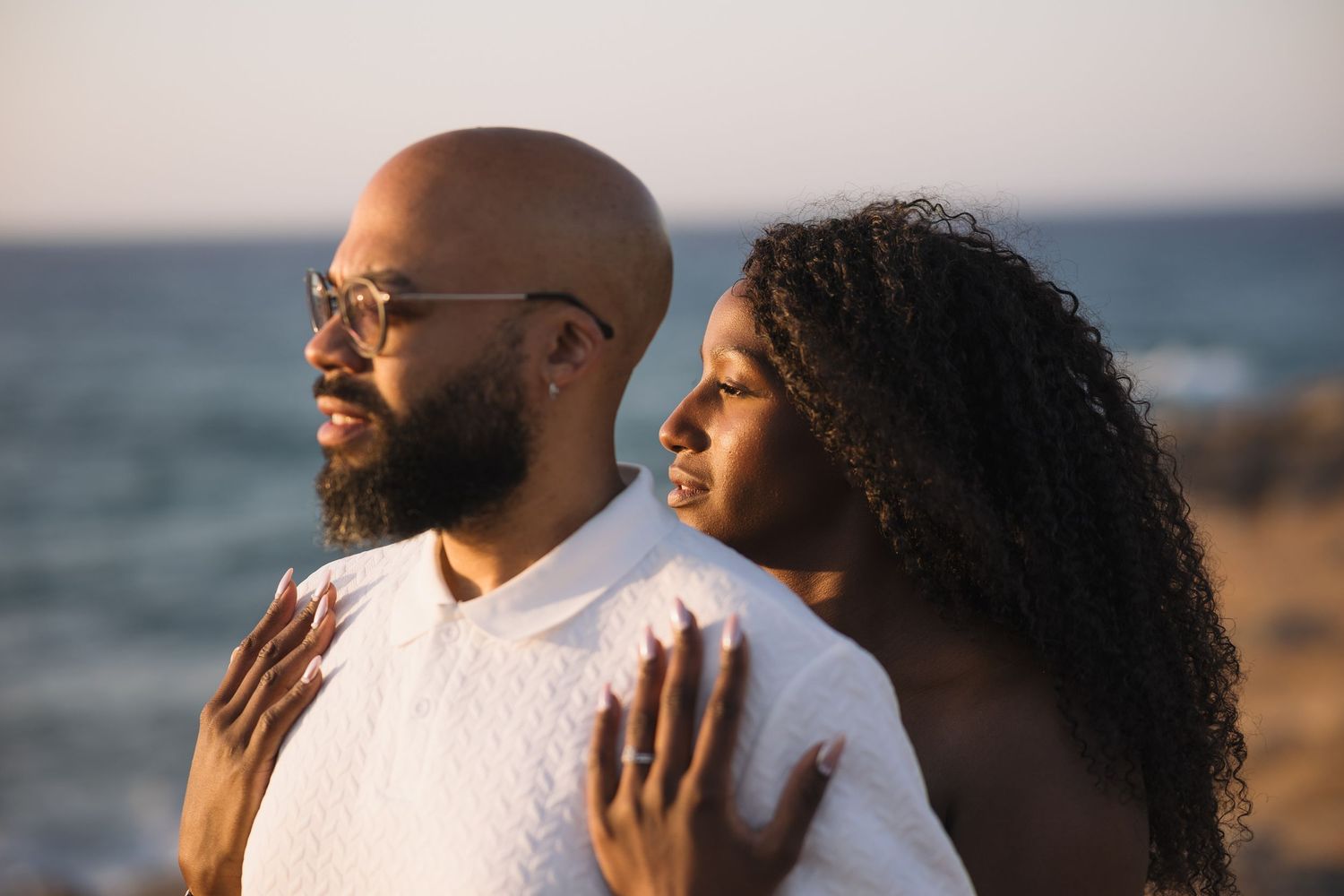 Couple embracing by ocean during golden hour photoshoot.