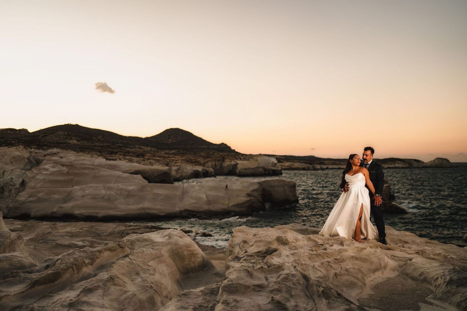 Couple photographed on rocky coastal cliffs during sunset.