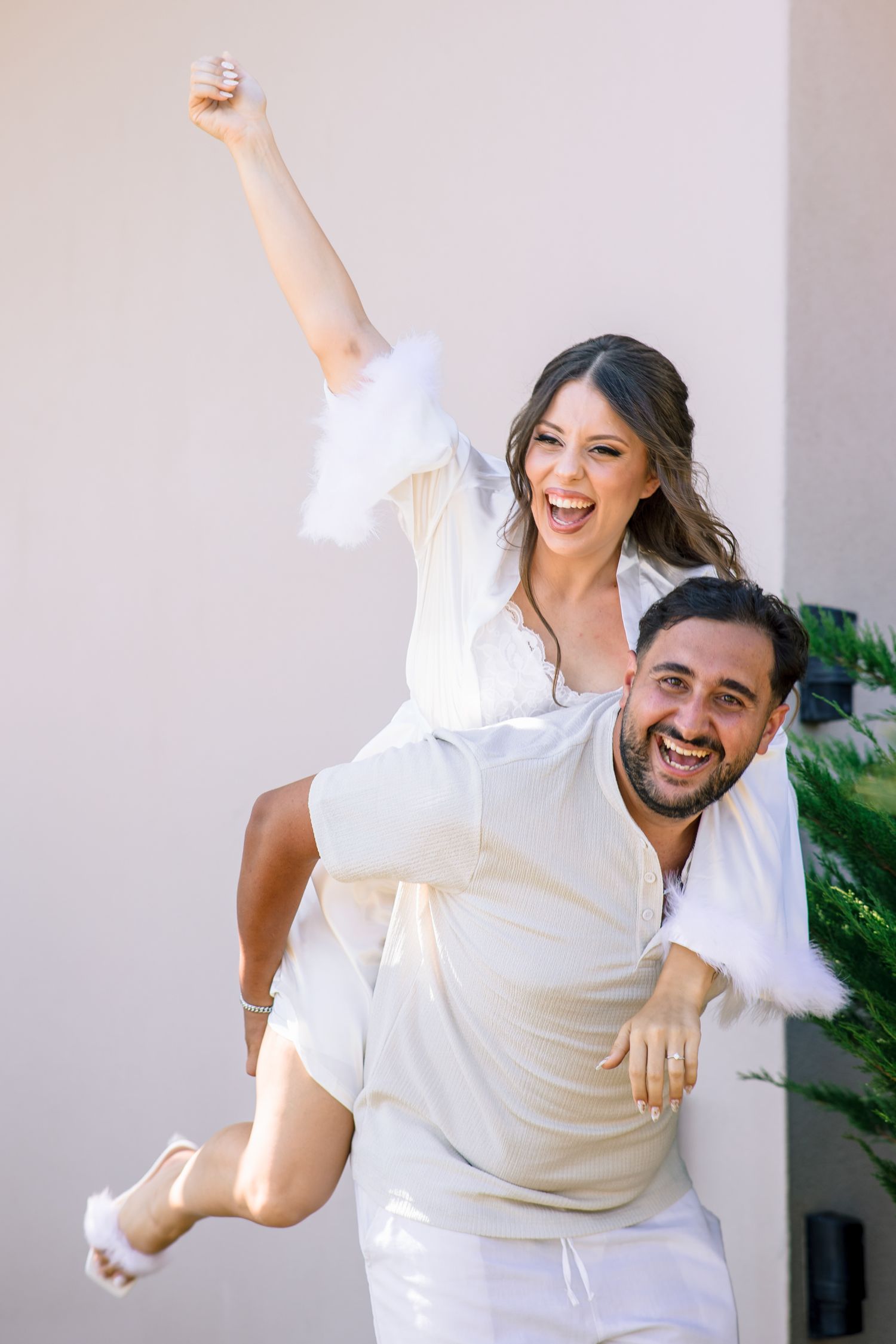 Couple in white outfits jumping and celebrating together against light background.