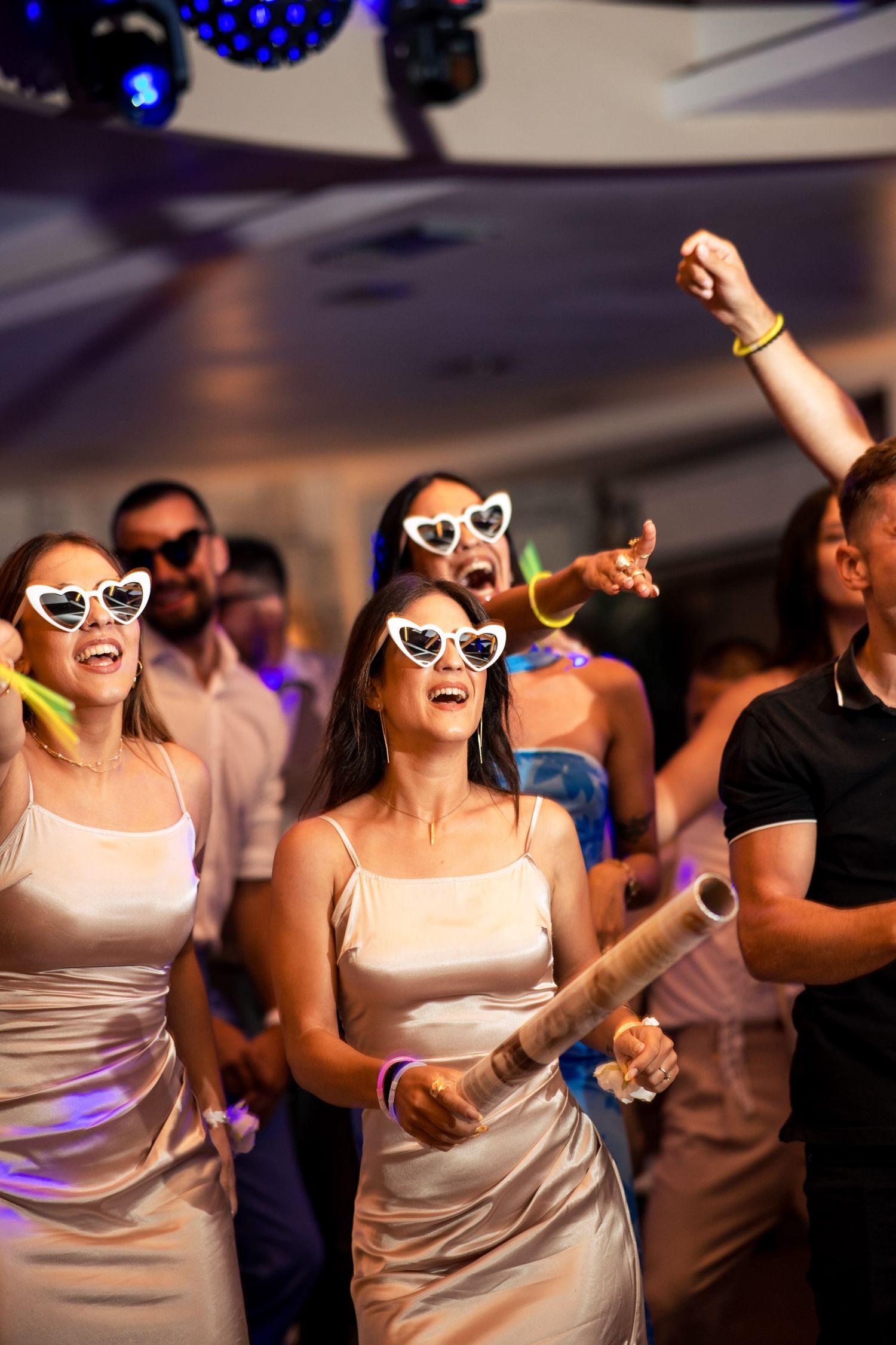 Wedding guests in white dresses and sunglasses dance joyfully at reception.