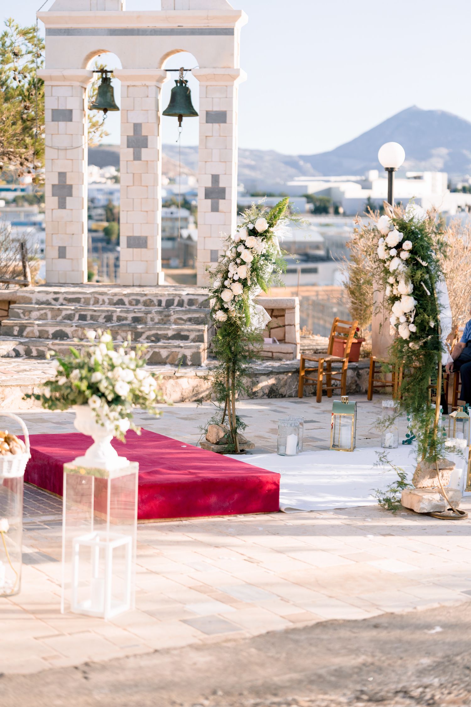 Outdoor wedding venue decorated with white flowers and red carpet path leading to an arched stone structure.