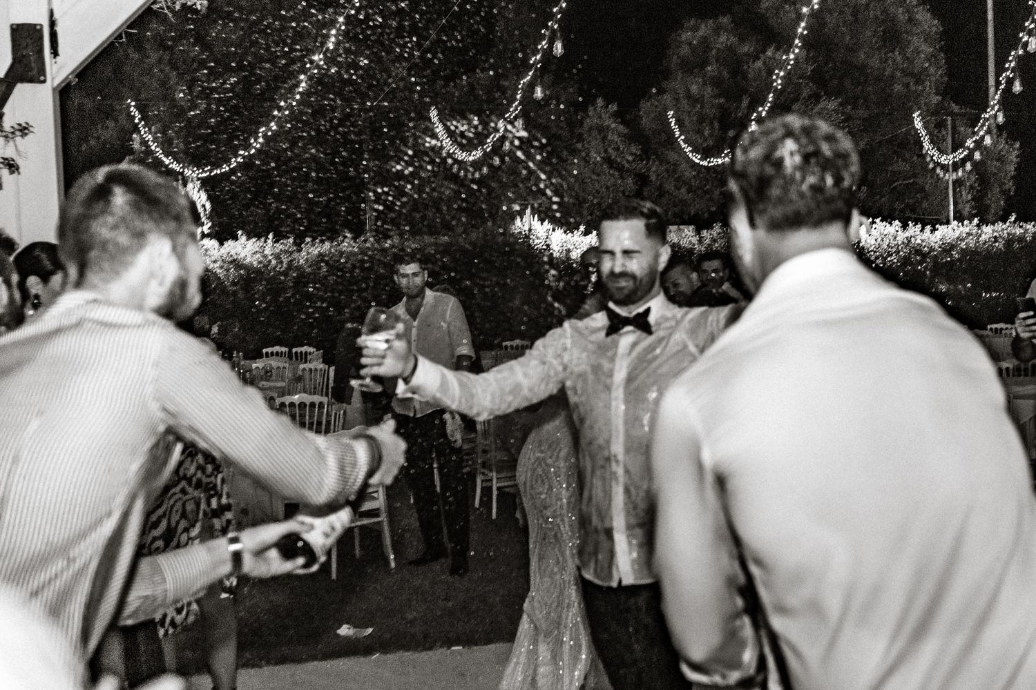 Black and white photo of guests celebrating with string lights decorating an outdoor party space.