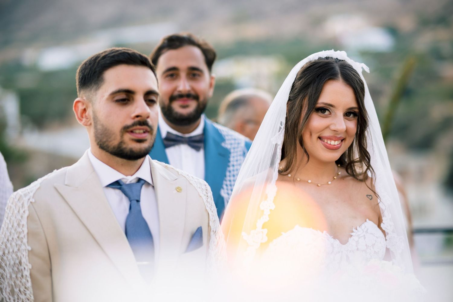Wedding party members in light colored suits and formal attire smiling outdoors.
