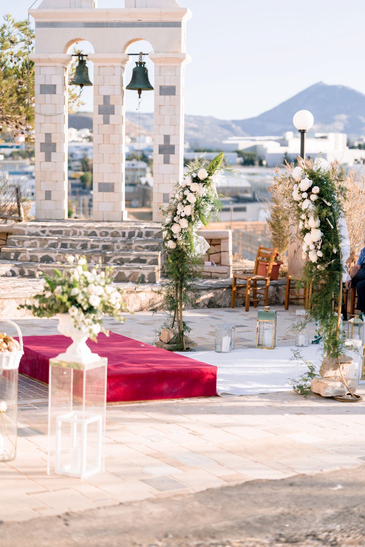 Outdoor wedding venue decorated with white floral arrangements and red carpet against mountain backdrop.
