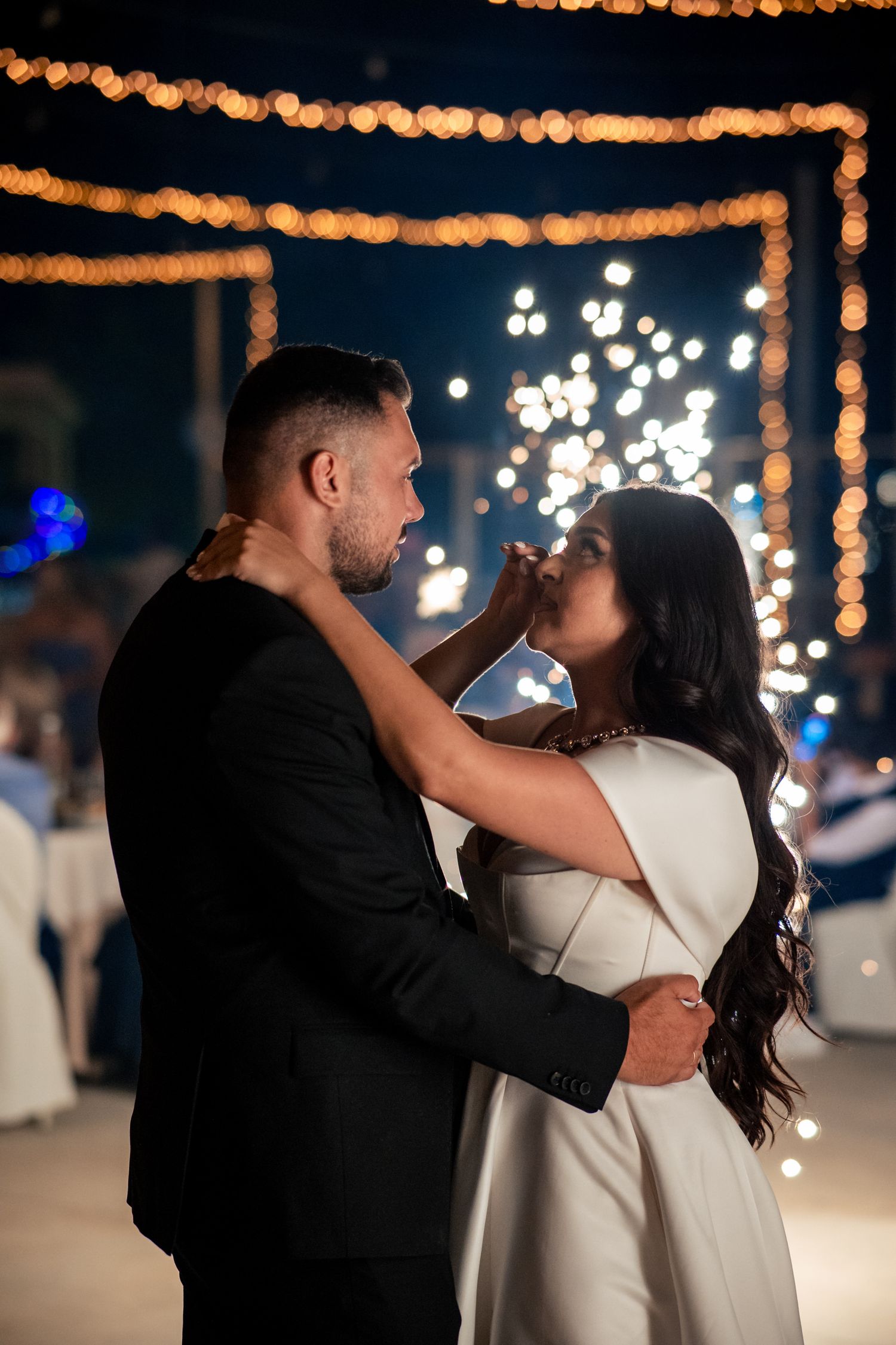 Couple dancing beneath warm string lights at nighttime celebration.