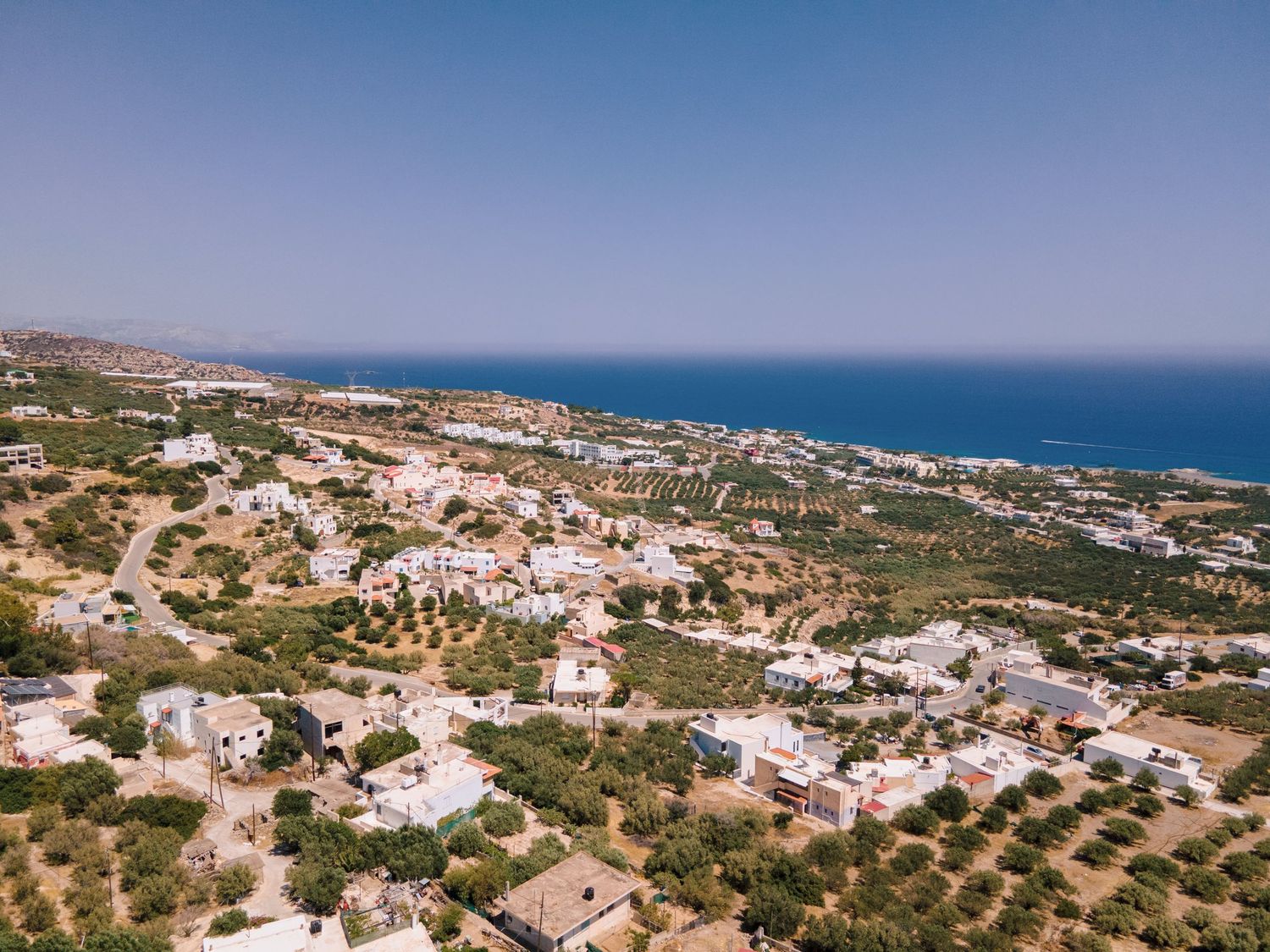 Aerial view of a coastal Mediterranean village with white buildings and blue sea.