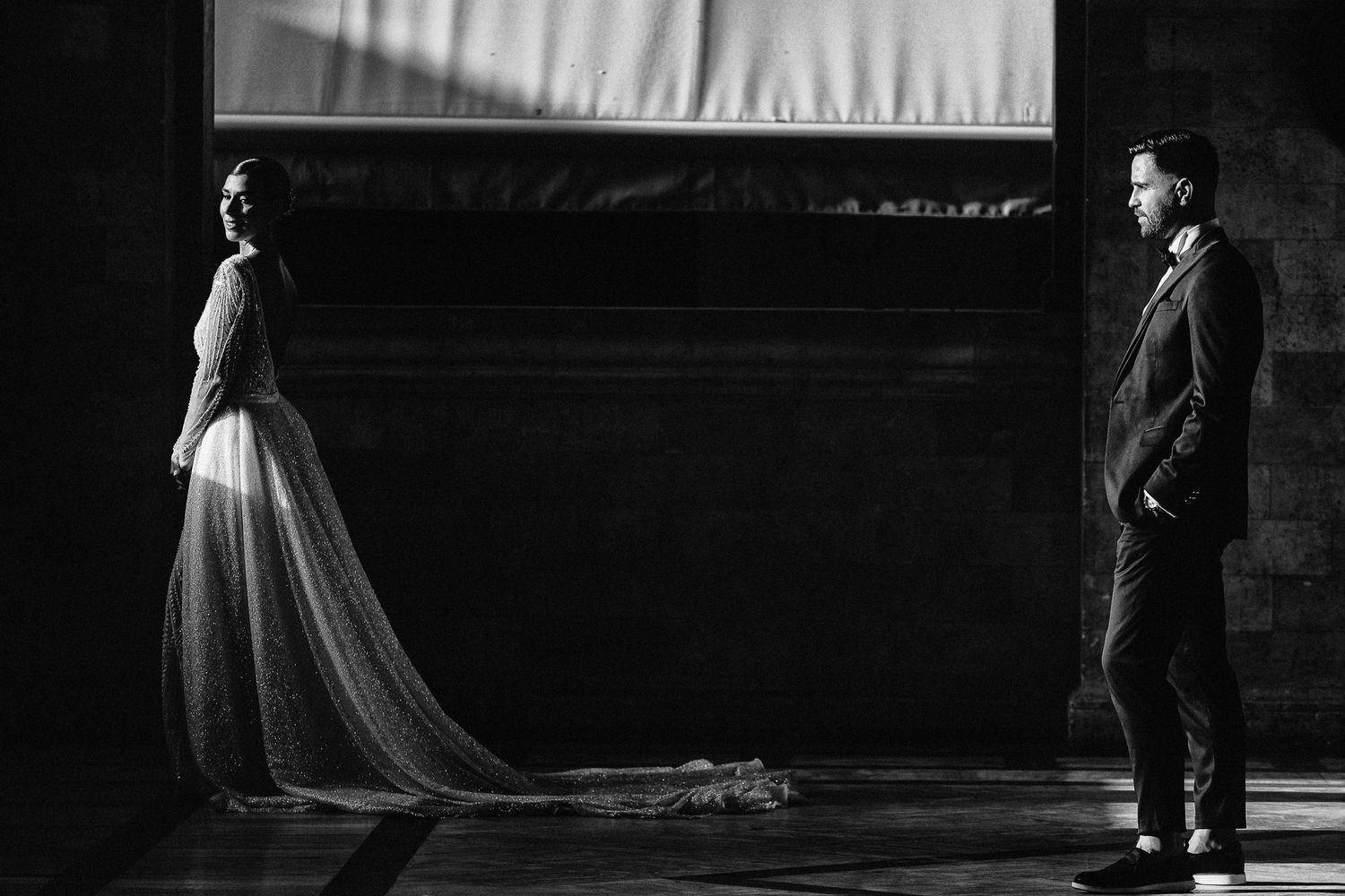 Dramatic black and white photo of couple standing apart in formal wedding attire.