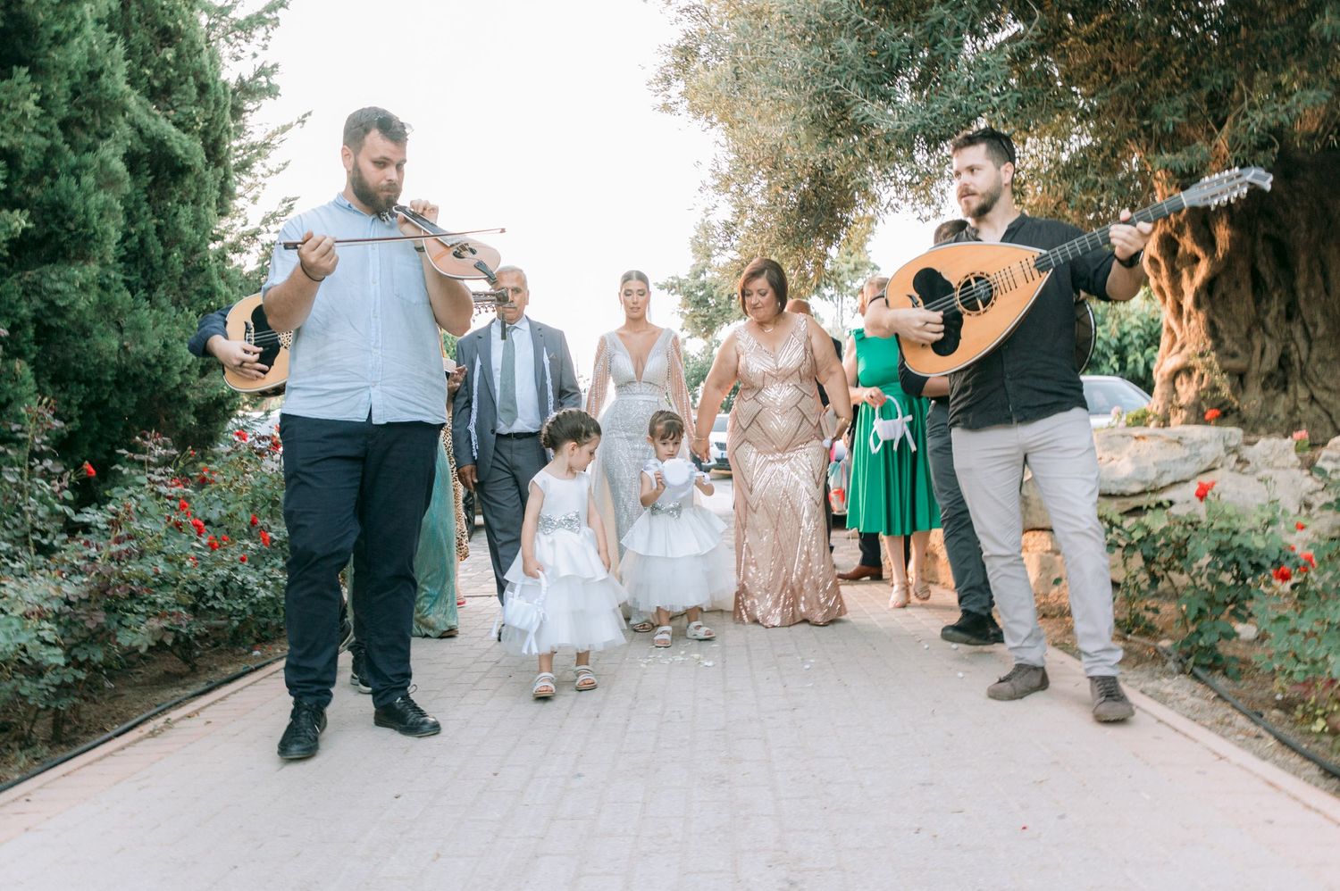 Wedding celebration procession walking along a garden path with musical instruments.