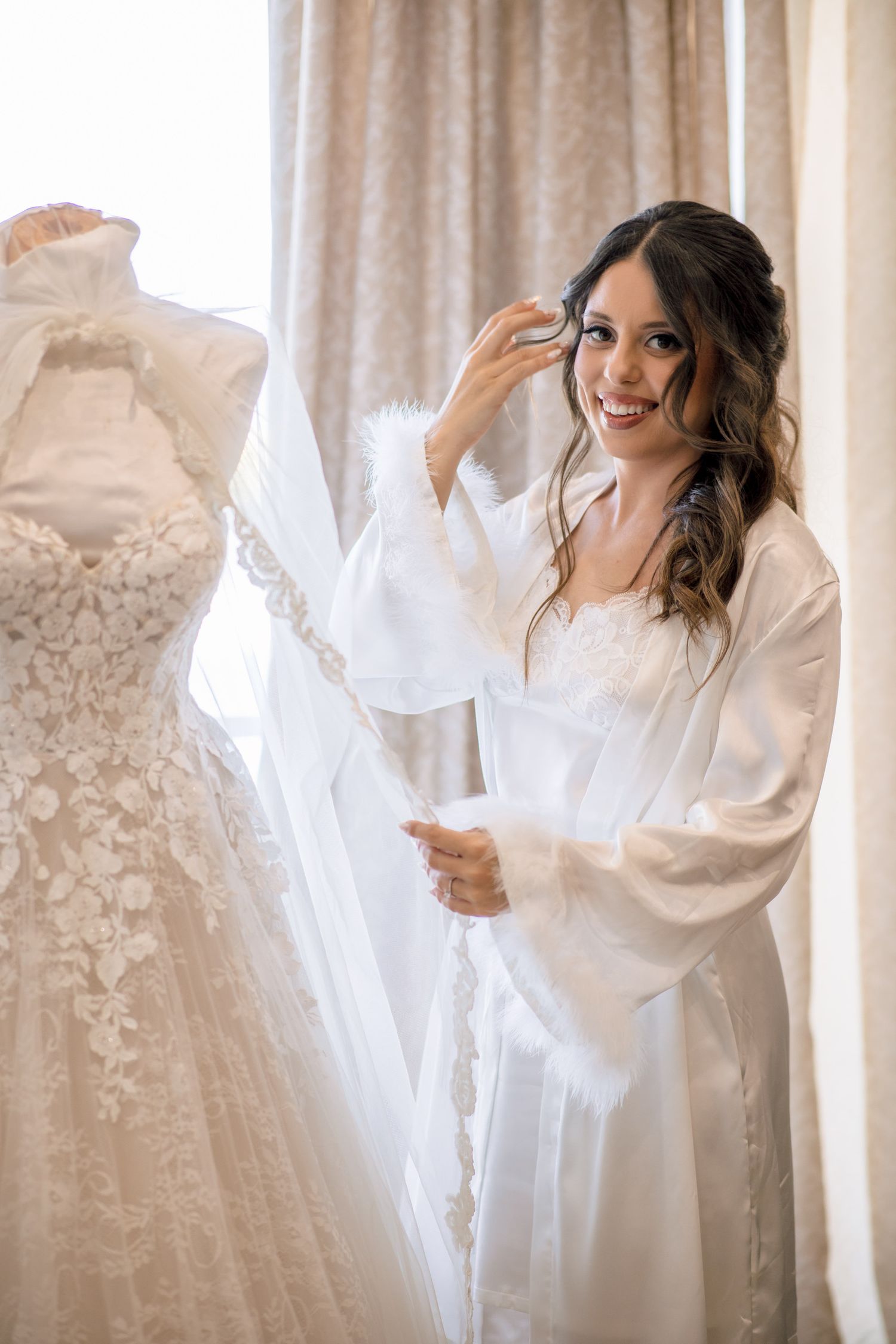 Elegant wedding gown with intricate details hanging by window.