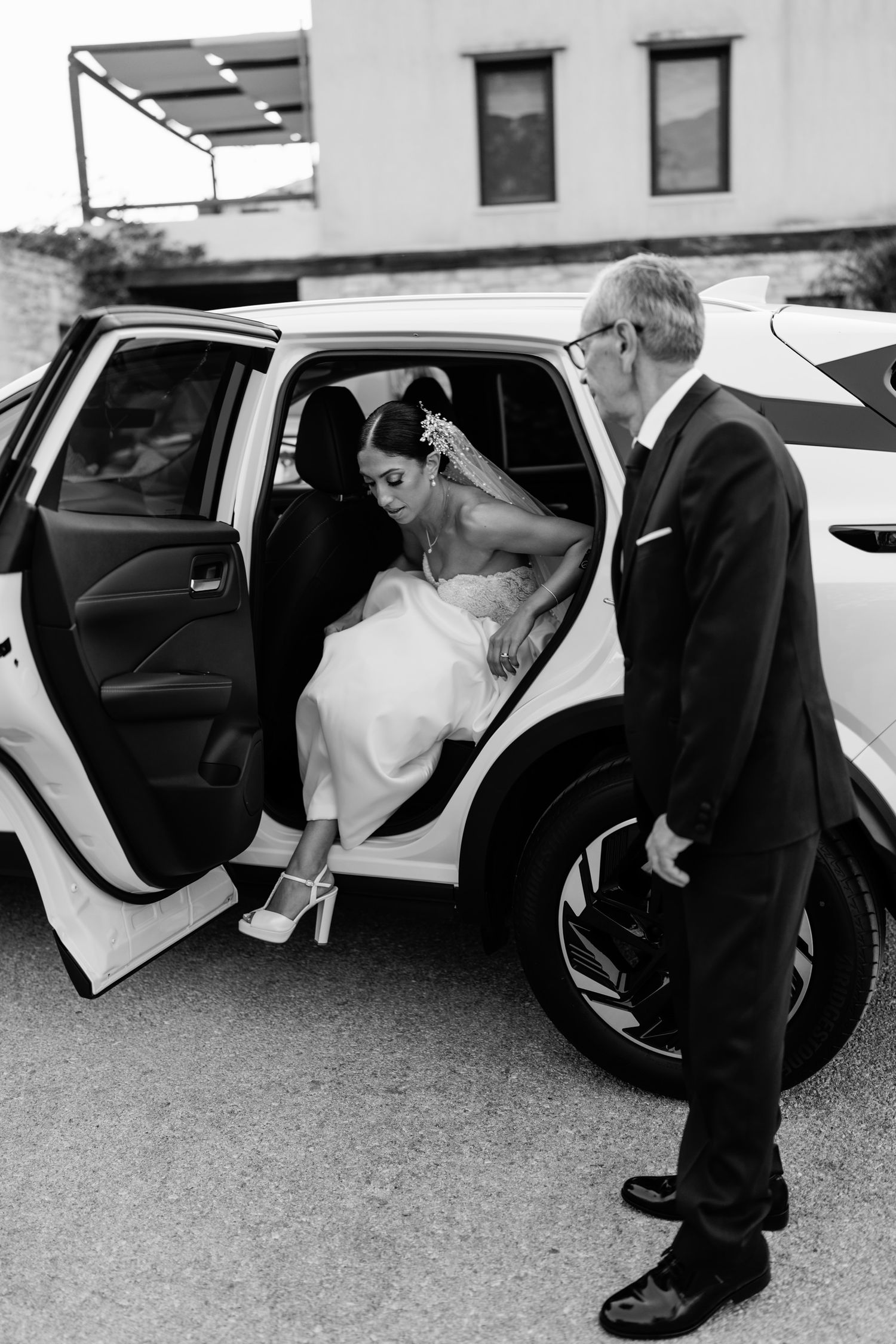 Black and white photo showing formal shoes and legs entering a luxury car.