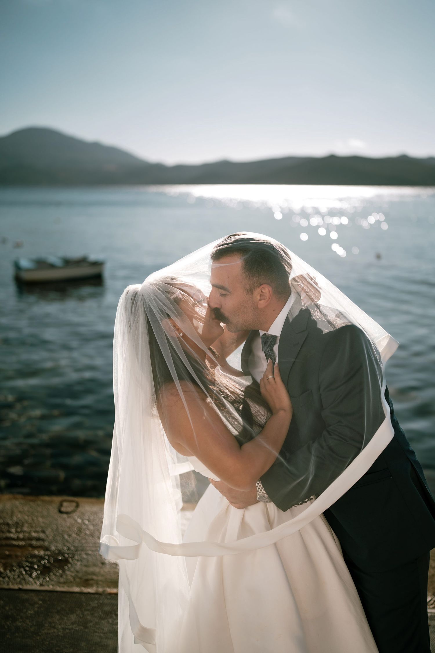 Intimate wedding moments captured under flowing veil by the seaside.
