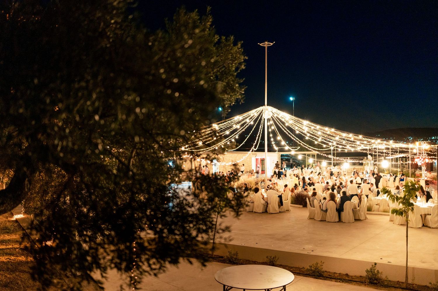 String lights illuminate an outdoor evening wedding reception under a tent.