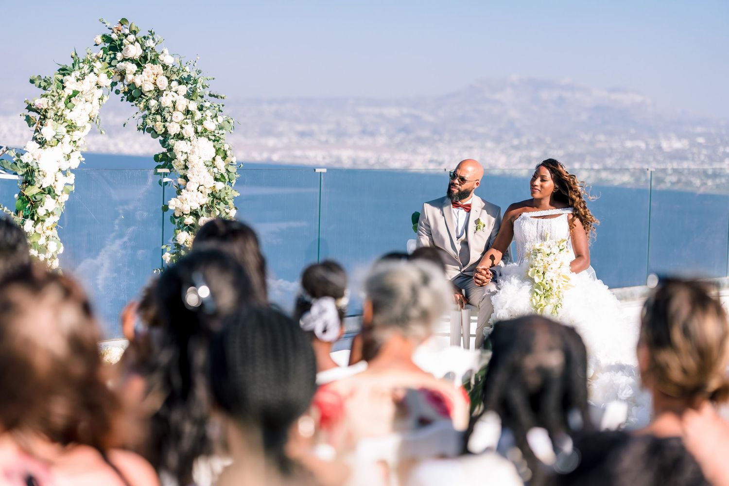 Outdoor wedding ceremony with floral arch and ocean view backdrop.