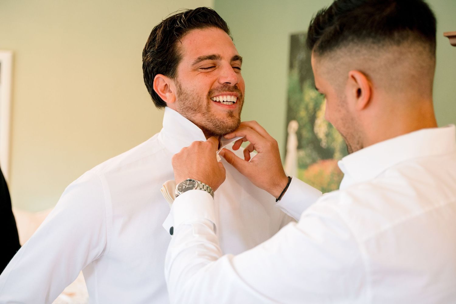 Groomsmen in white dress shirts share laughs and smiles while getting ready.
