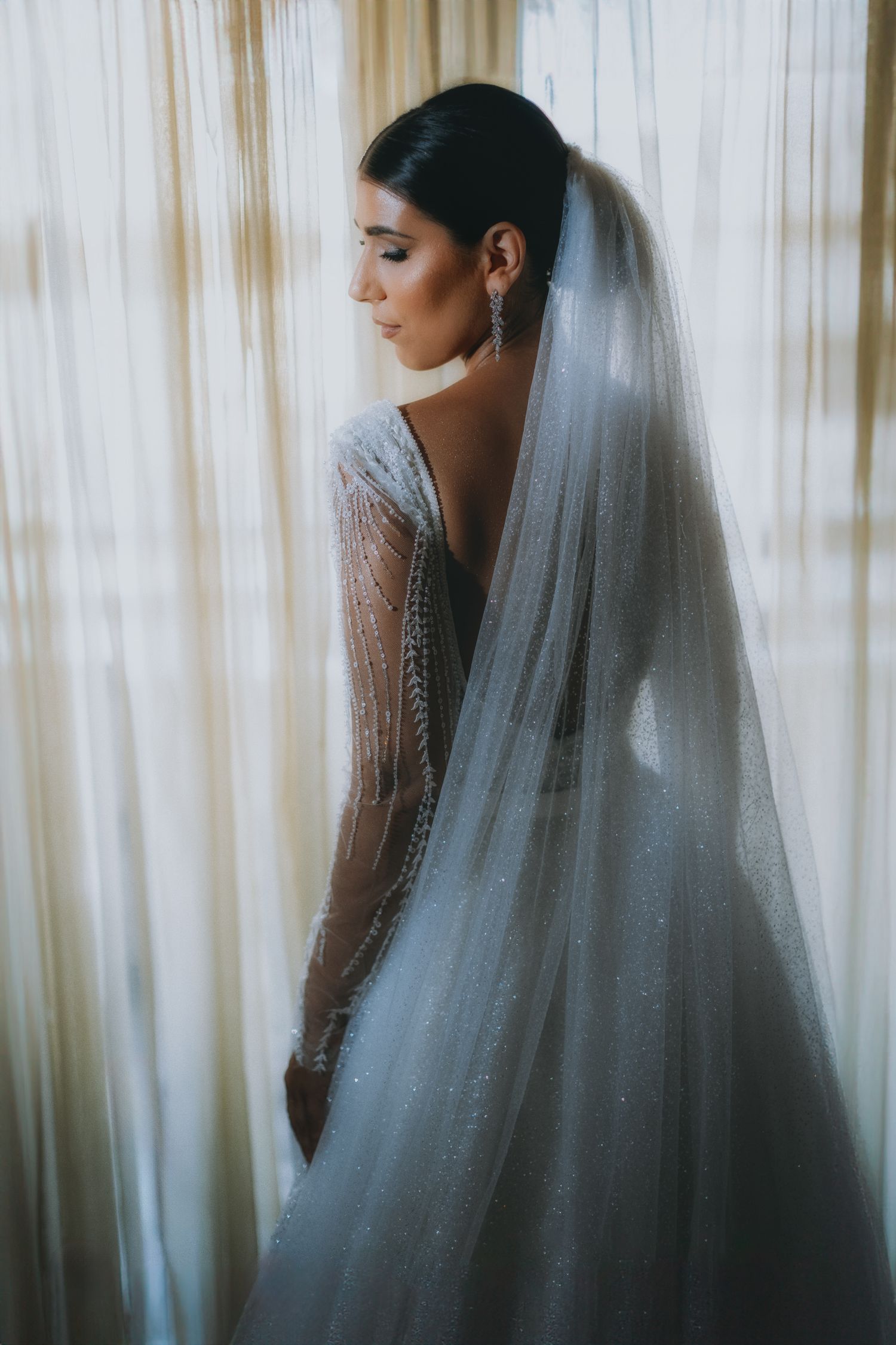 Ethereal bridal portrait through sheer curtains showing a delicate veil and gown silhouette.