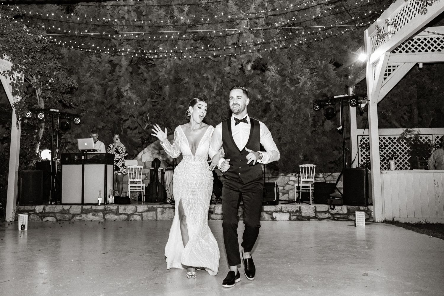 Wedding guests dancing on an outdoor patio with decorative lighting and stone walls.
