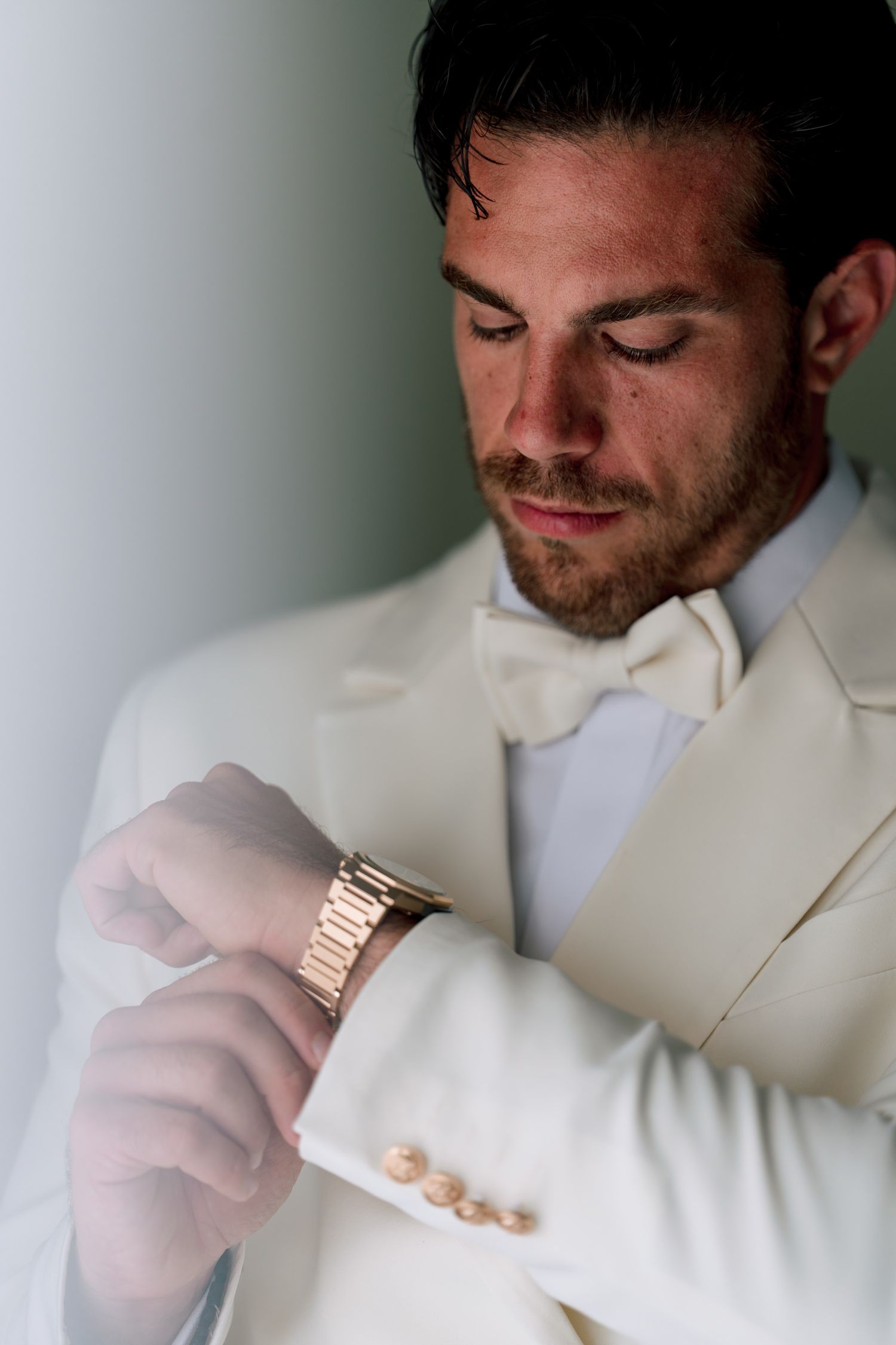 Close-up detail of a gold watch on a white suit sleeve.
