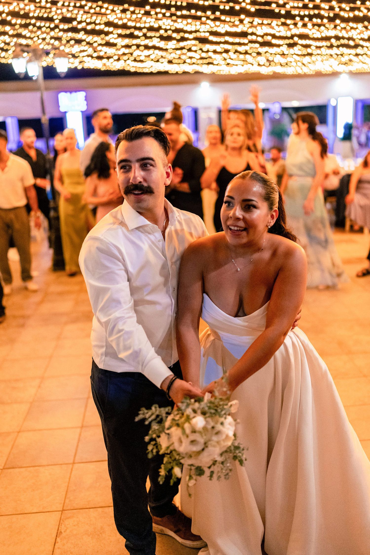 A couple shares a playful dance moment under warm string lights at their wedding reception.