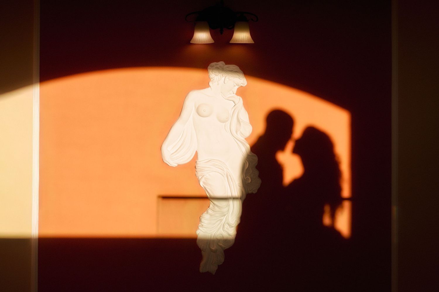 Silhouettes against a warm orange sunset sky create a dramatic panoramic view through arched windows.