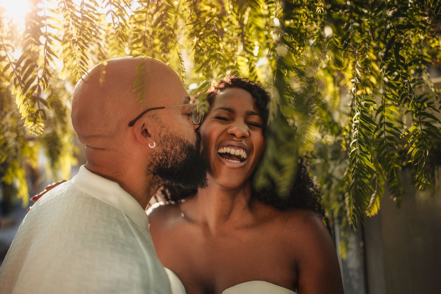 Joyful couple embracing under illuminated yellow leaves at outdoor event.