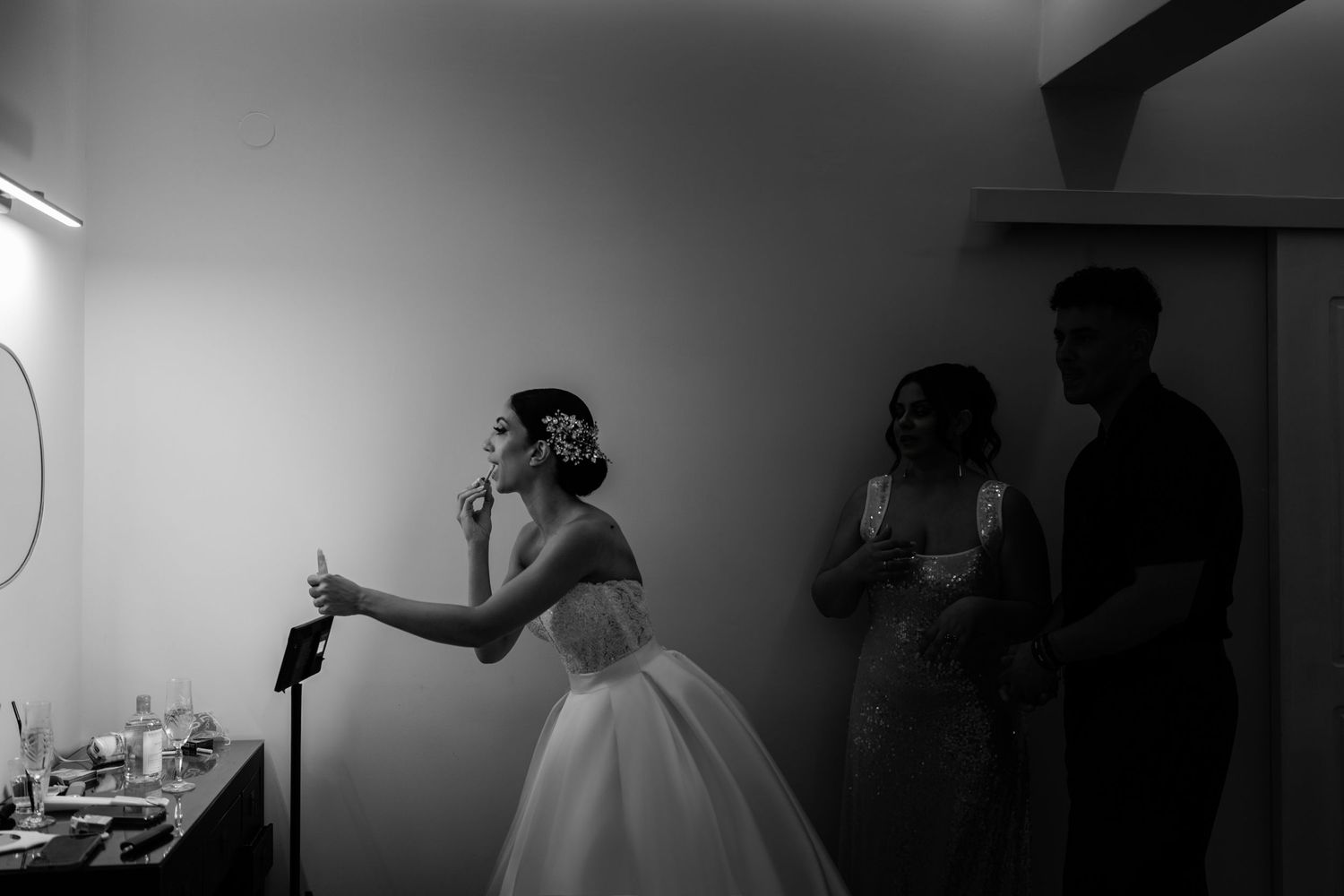 Silhouetted figures prepare in a dimly lit room before the wedding ceremony.