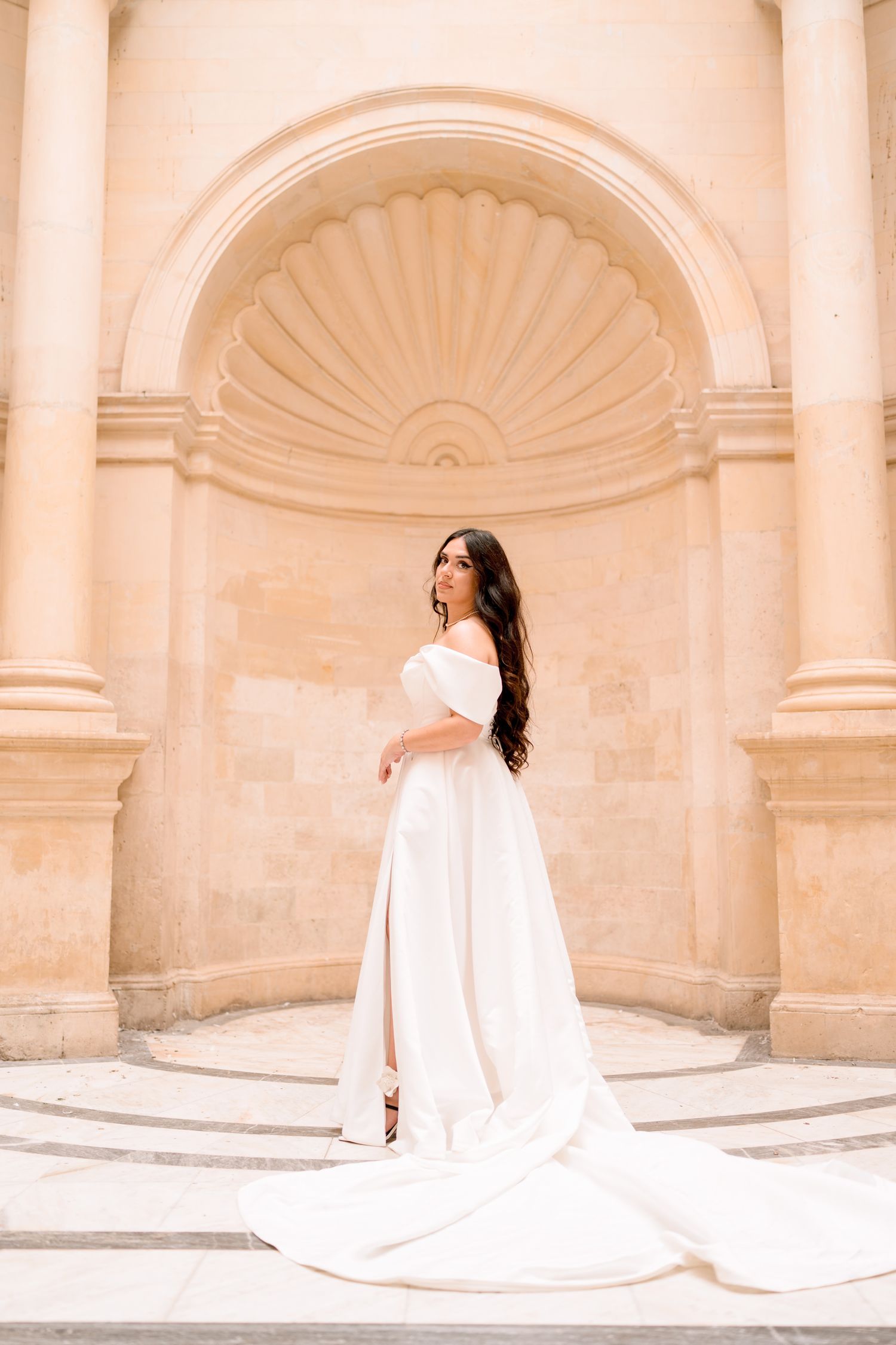A bride in a flowing white gown poses in a series against cream-colored classical architecture.