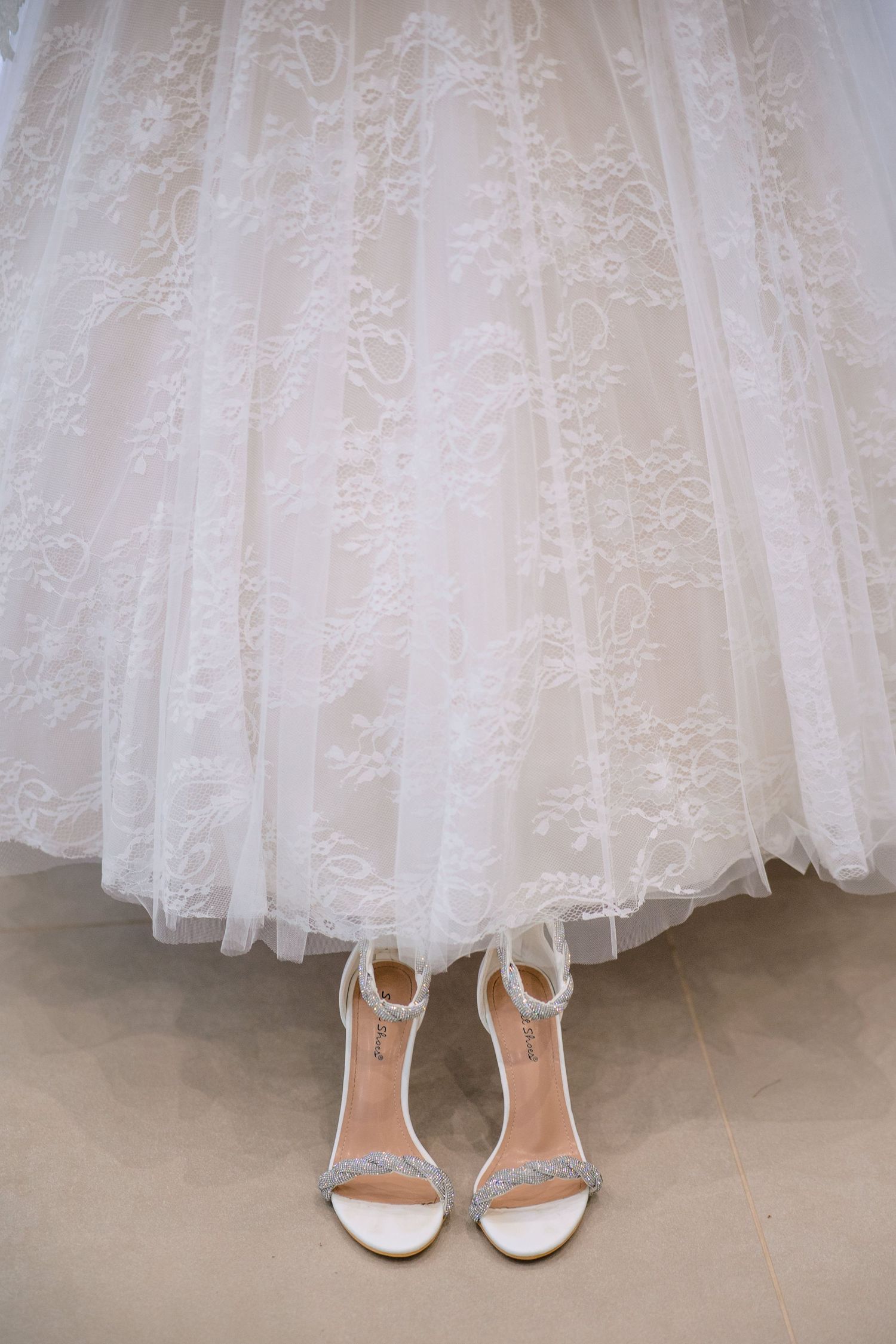 Close-up view of elegant white bridal shoes peeking out beneath layers of delicate lace wedding dress tulle.
