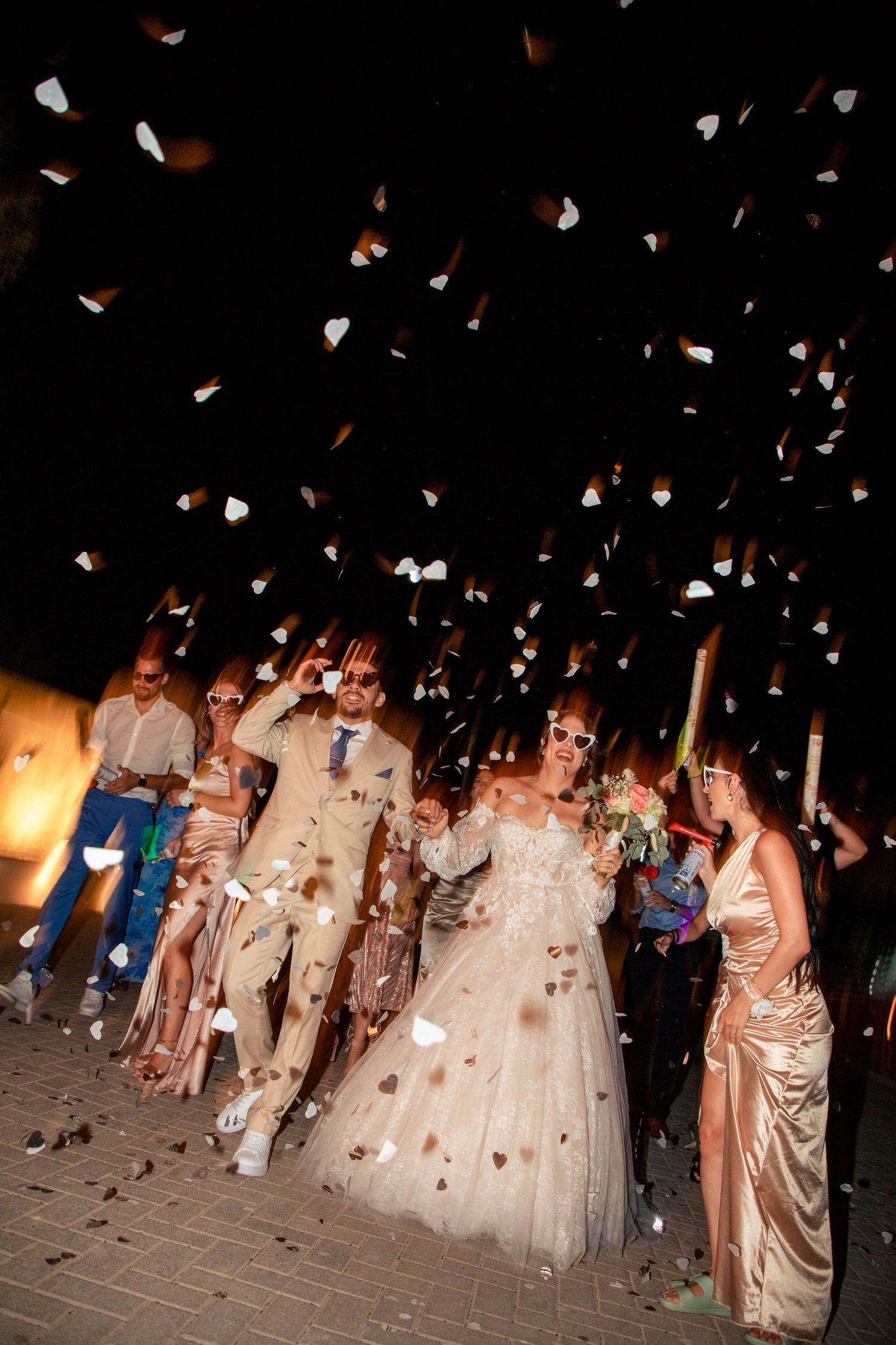 Wedding party celebrates with confetti toss at night during outdoor reception celebration.