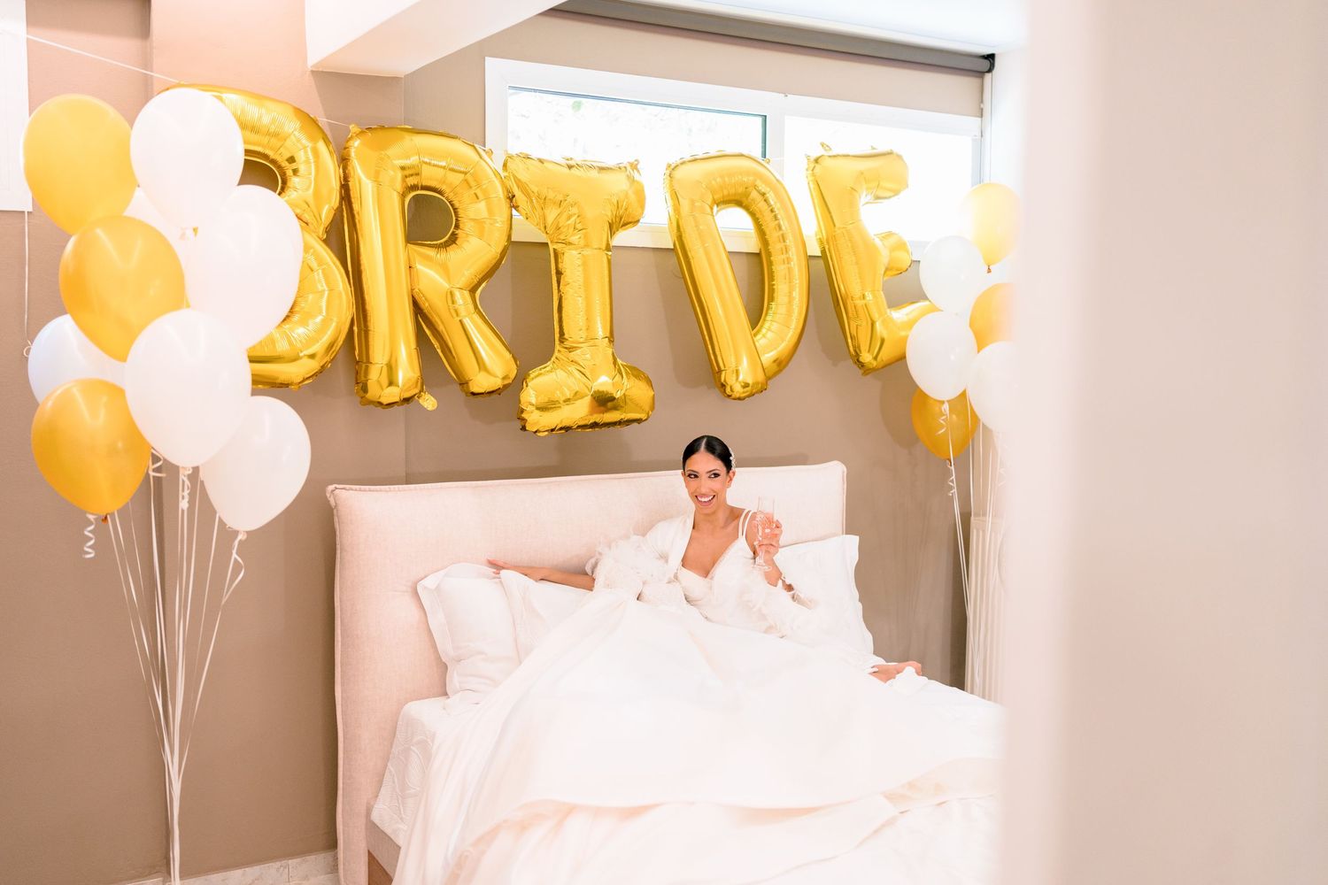 Gold 'BRIDE' balloons and white decorations in a bridal preparation room.
