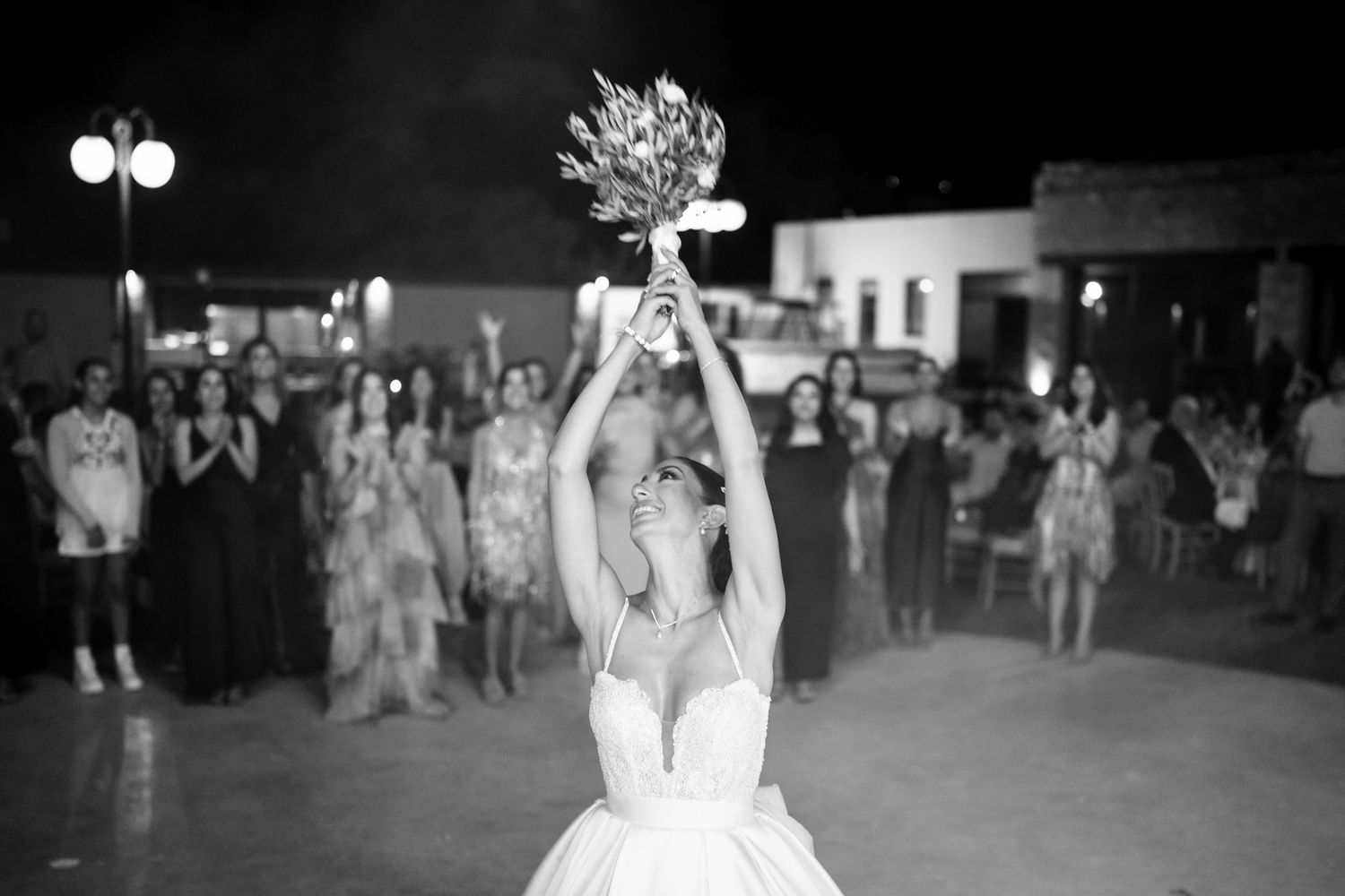 Black and white photo of a wedding bouquet toss with crowd watching in background.