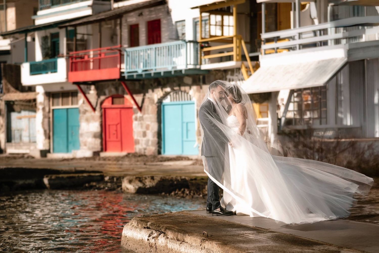 A flowing wedding veil catches the breeze along colorful waterfront buildings.