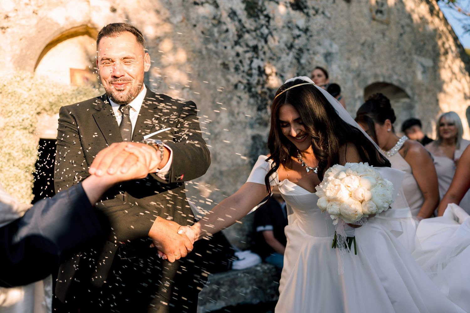 Sunlit wedding celebration with guests throwing confetti in warm afternoon light.