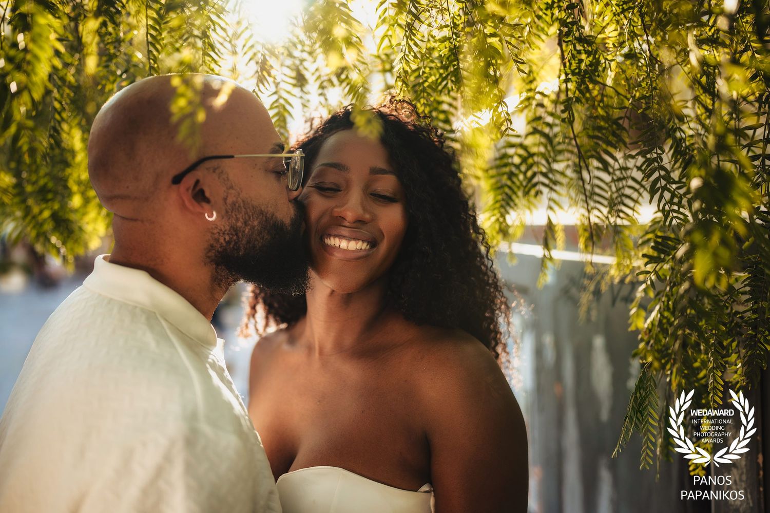 Intimate wedding couple moment under sunlit hanging foliage.