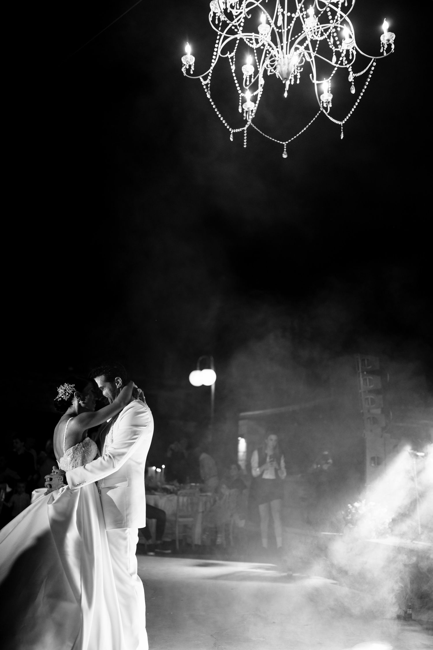 Elegant couple shares an intimate dance under a crystal chandelier in black and white.