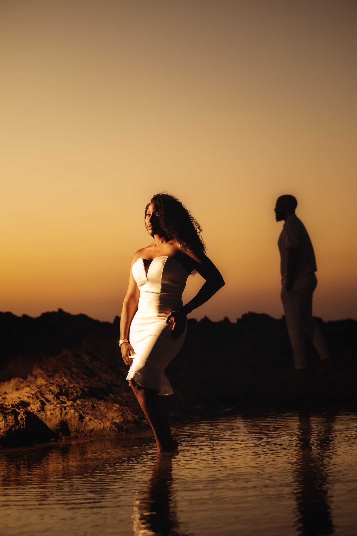 Dramatic sunset photoshoot with couple posing by water's edge.