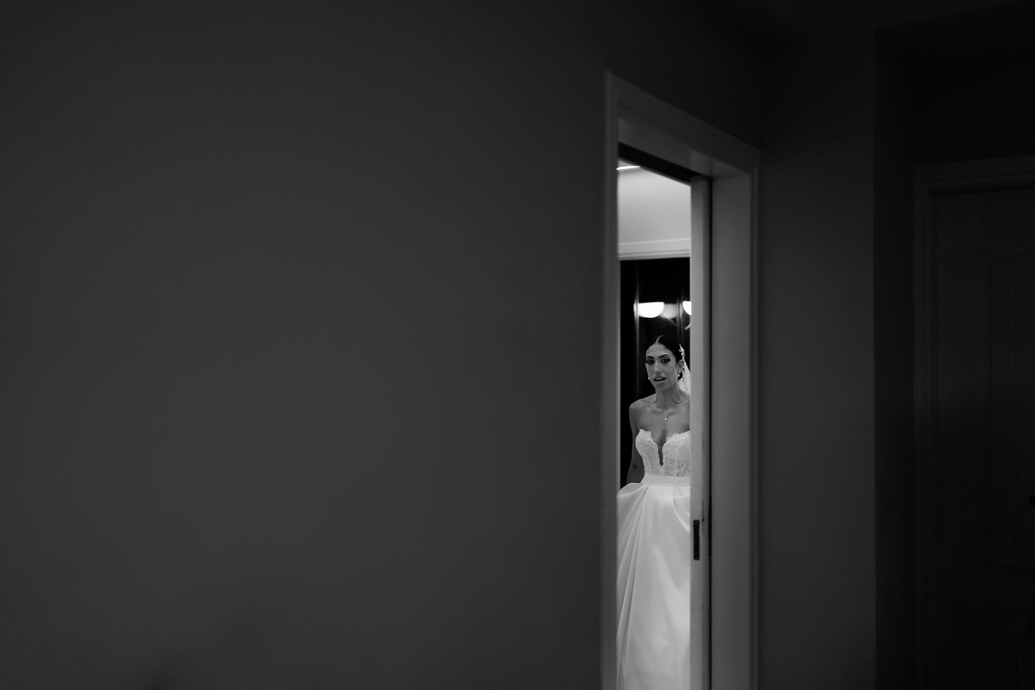 Moody black and white corridor shot with wedding dress in doorway.